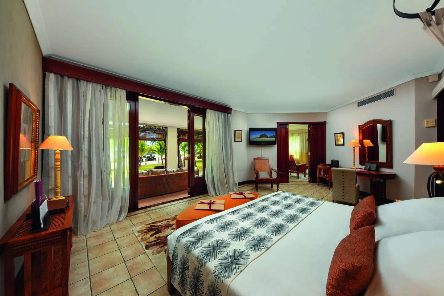 dinarobin senior suite bedroom with king bed, elegant tropical decor, and seating area