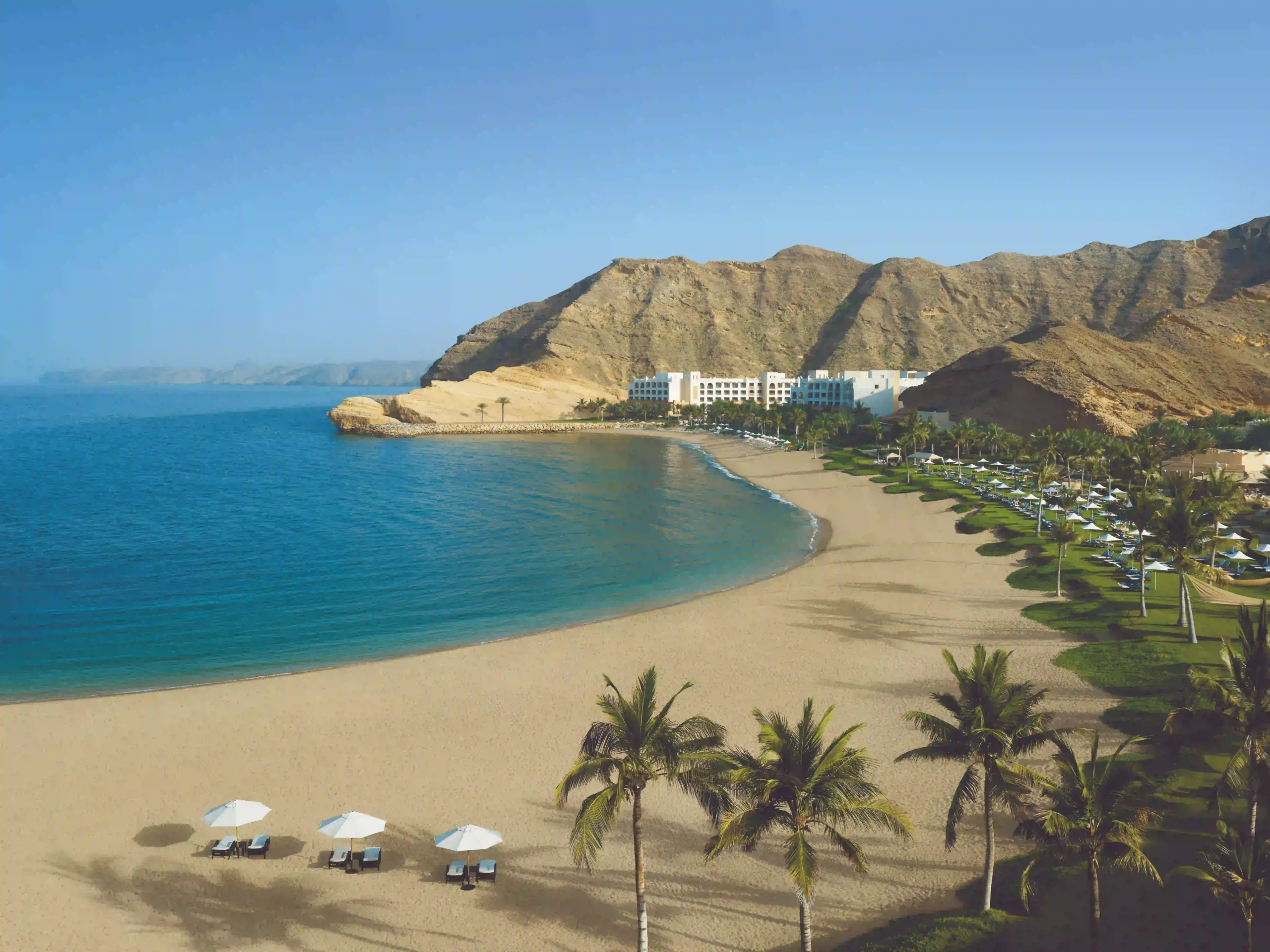 shangri-la oman beachfront with sun loungers and palm trees