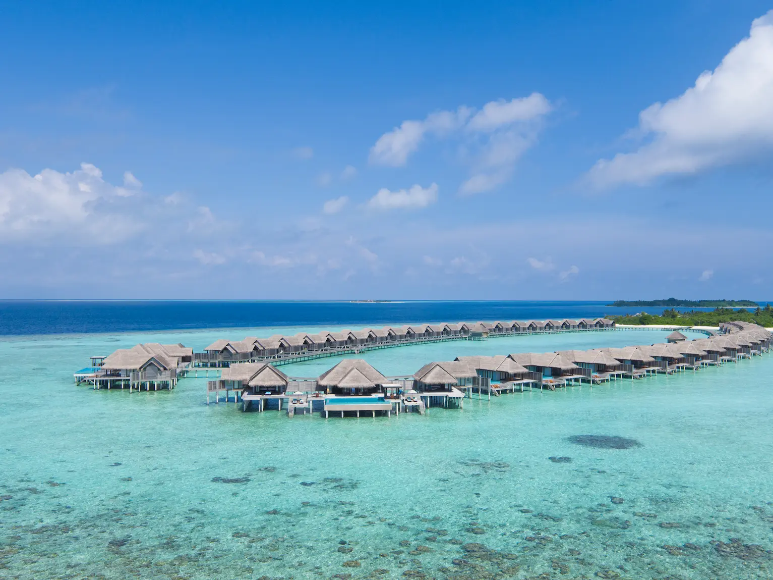 drone view of the overwater suites at anantara kihavah maldives villas set above crystal clear lagoon waters