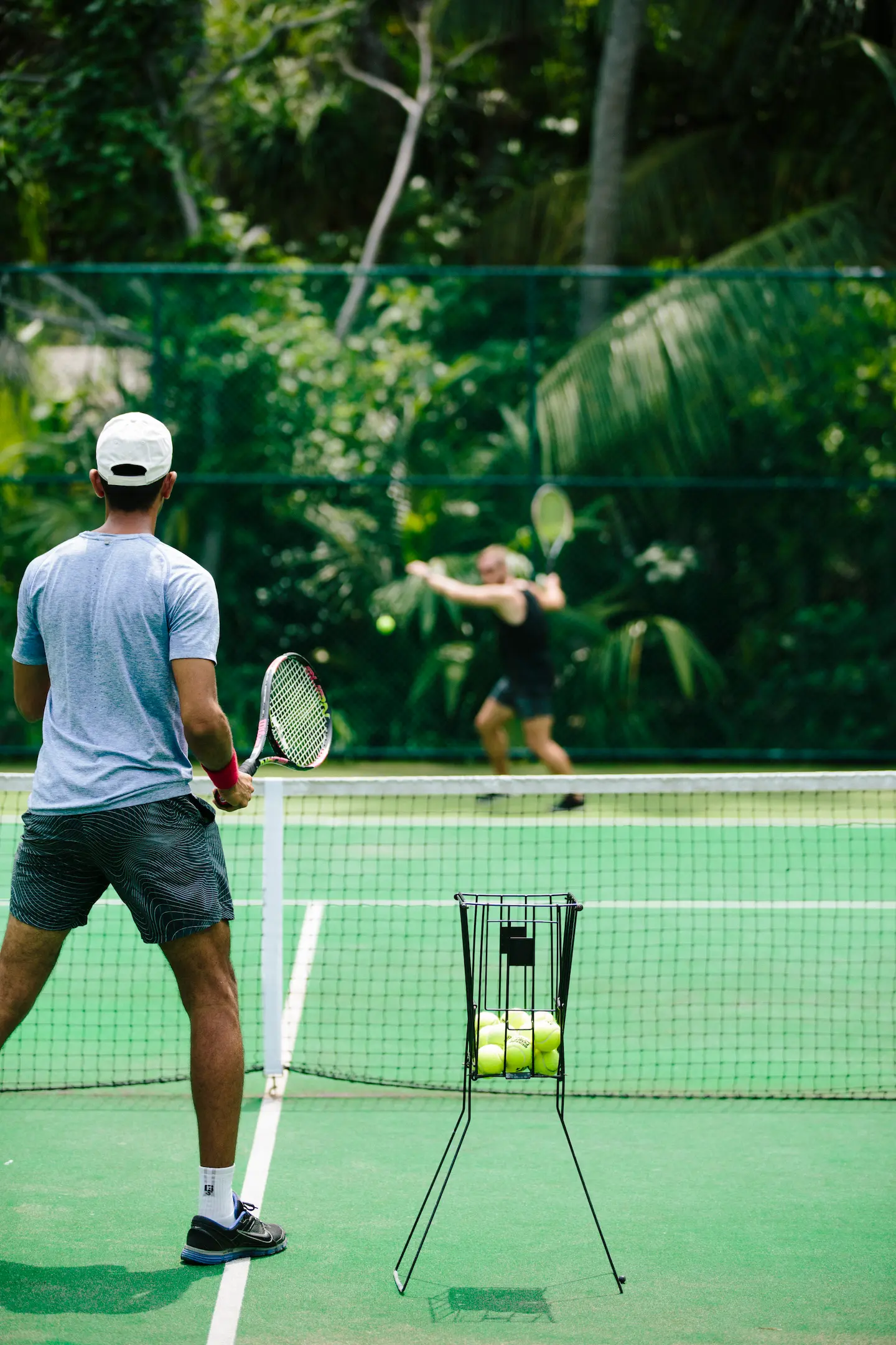 guests enjoying a match on the tennis court at anantara kihavah maldives villas surrounded by lush tropical greenery