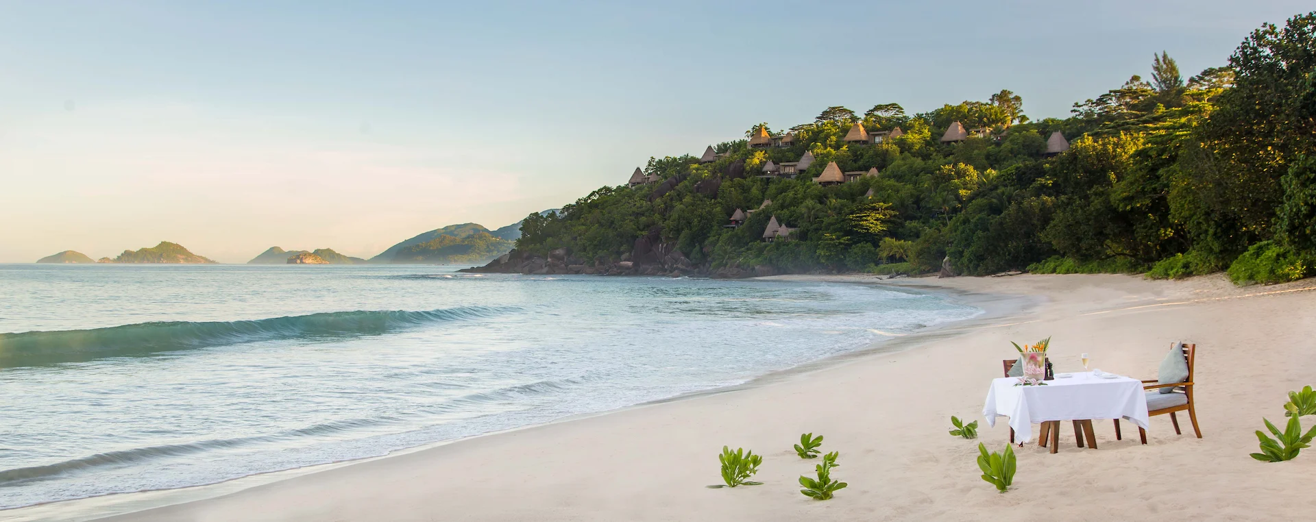 beach dinner setup at Anantara Maia Seychelles Villas with tables arranged on the sand overlooking the ocean at sunset