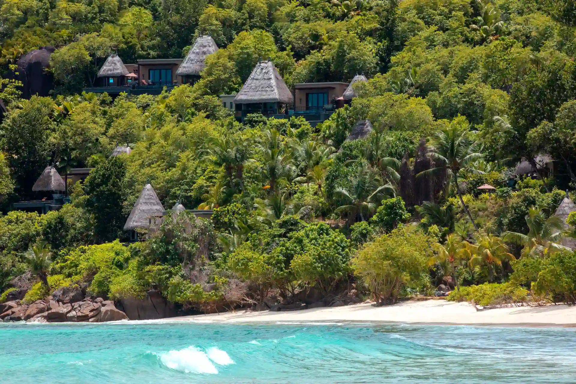 beach view at Anantara Maia Seychelles Villas with white sand, turquoise waters, and lush tropical greenery along the shoreline