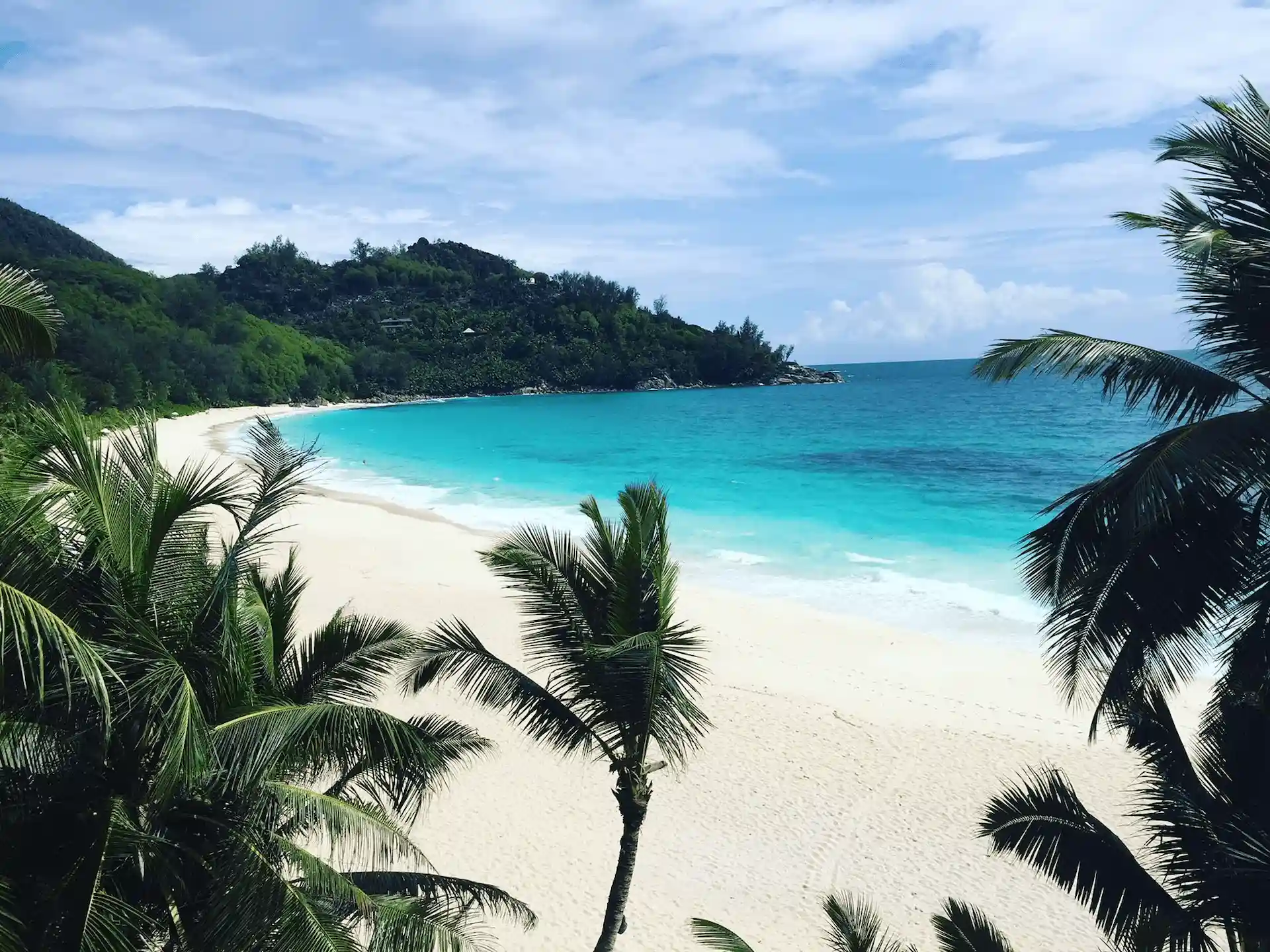 carana beach in seychelles with white sand shoreline, turquoise sea, and granite rocks along the coast
