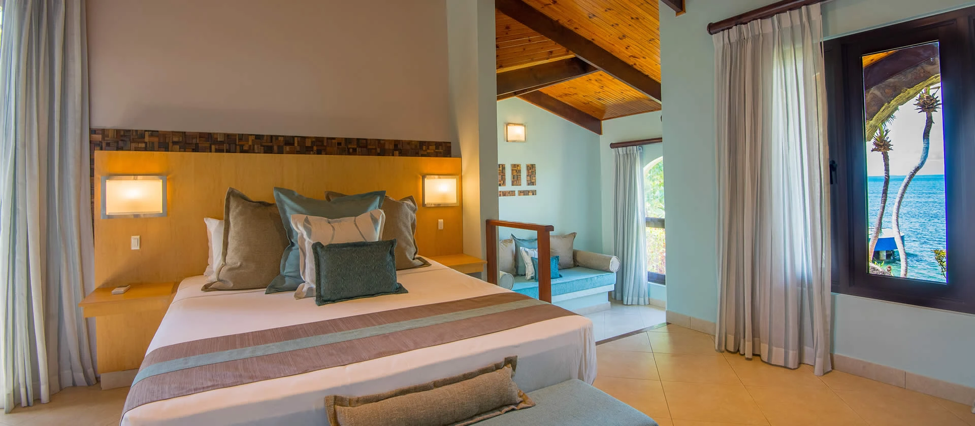 coco de mer seychelles standard room bed with king size mattress, tropical décor, and views of garden or ocean from windows