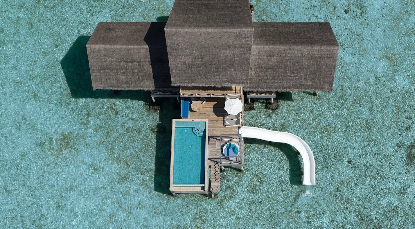 cora cora maldives two bedroom lagoon pool villa with slide shown in an aerial view over the turquoise lagoon and overwater luxury setting