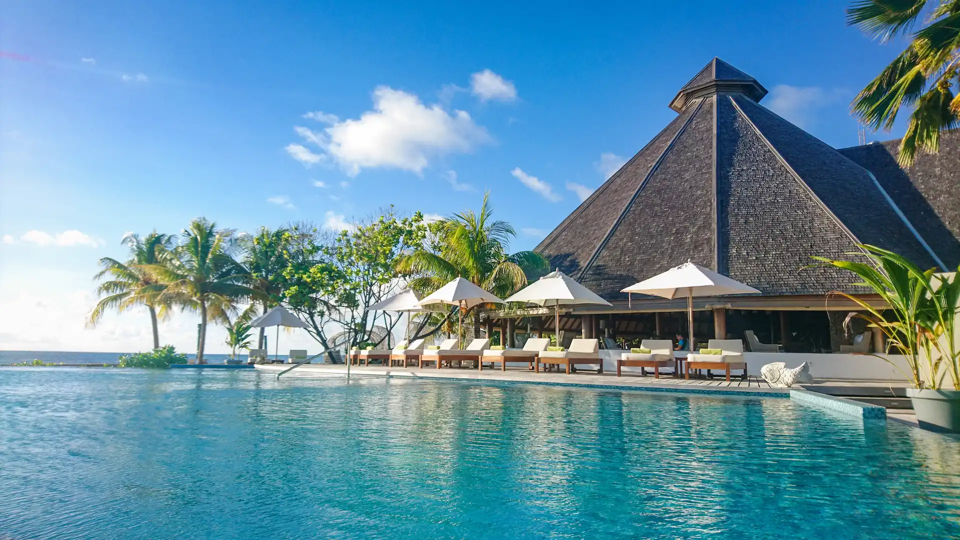 denis private island seychelles pool area adjacent to main building with sun loungers, tropical landscaping, and panoramic ocean views
