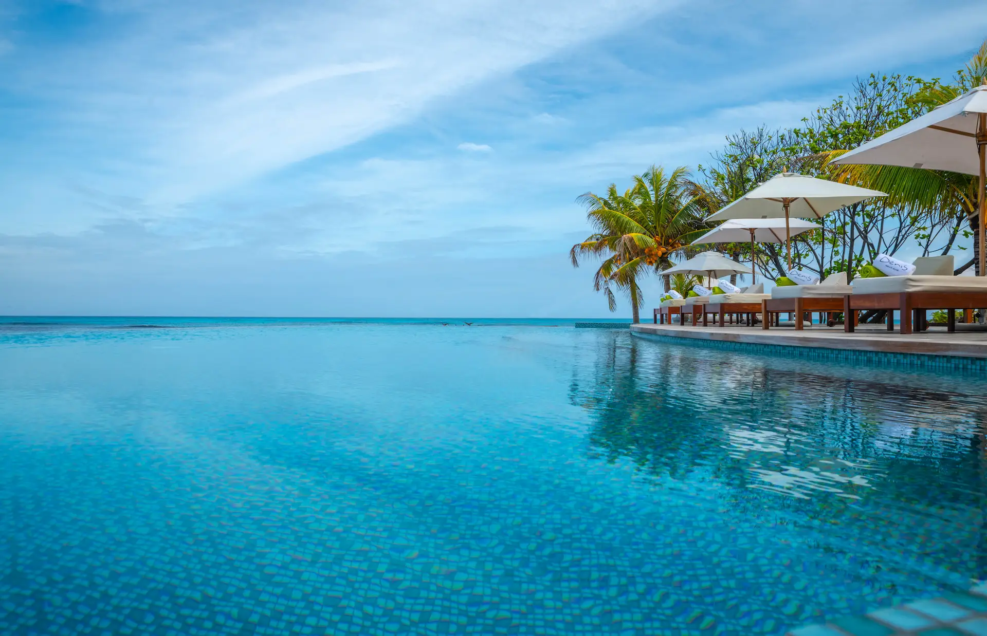 denis private island seychelles swimming pool with sun loungers, tropical landscaping, and panoramic views of the turquoise ocean and white