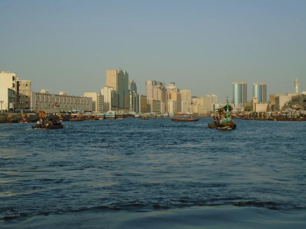traditional wooden abra boats crossing dubai creek with passengers on board and historic buildings along the waterfront