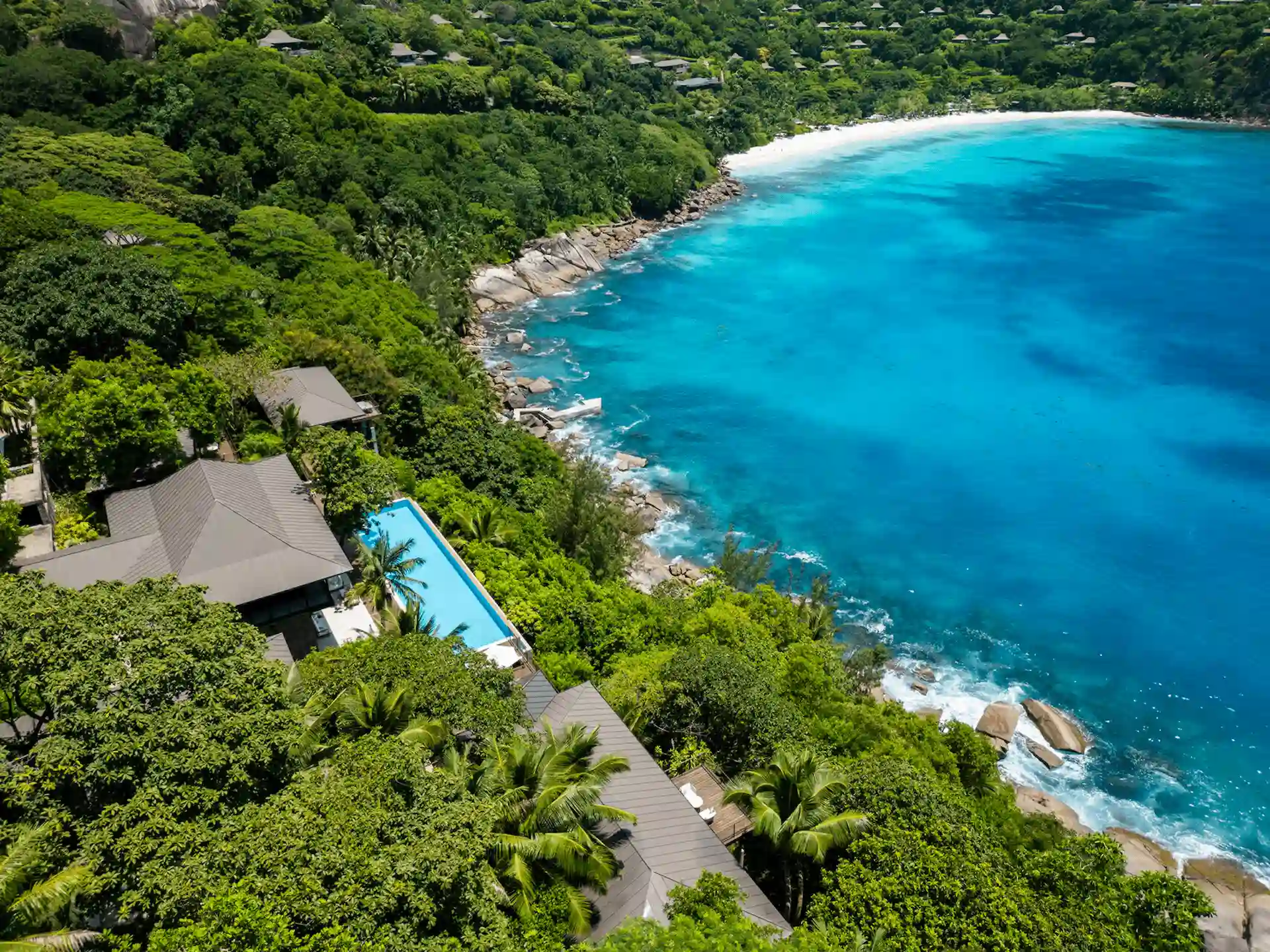 secluded cove at Four Seasons Resort Seychelles with calm turquoise waters, rocky shoreline, and tropical greenery