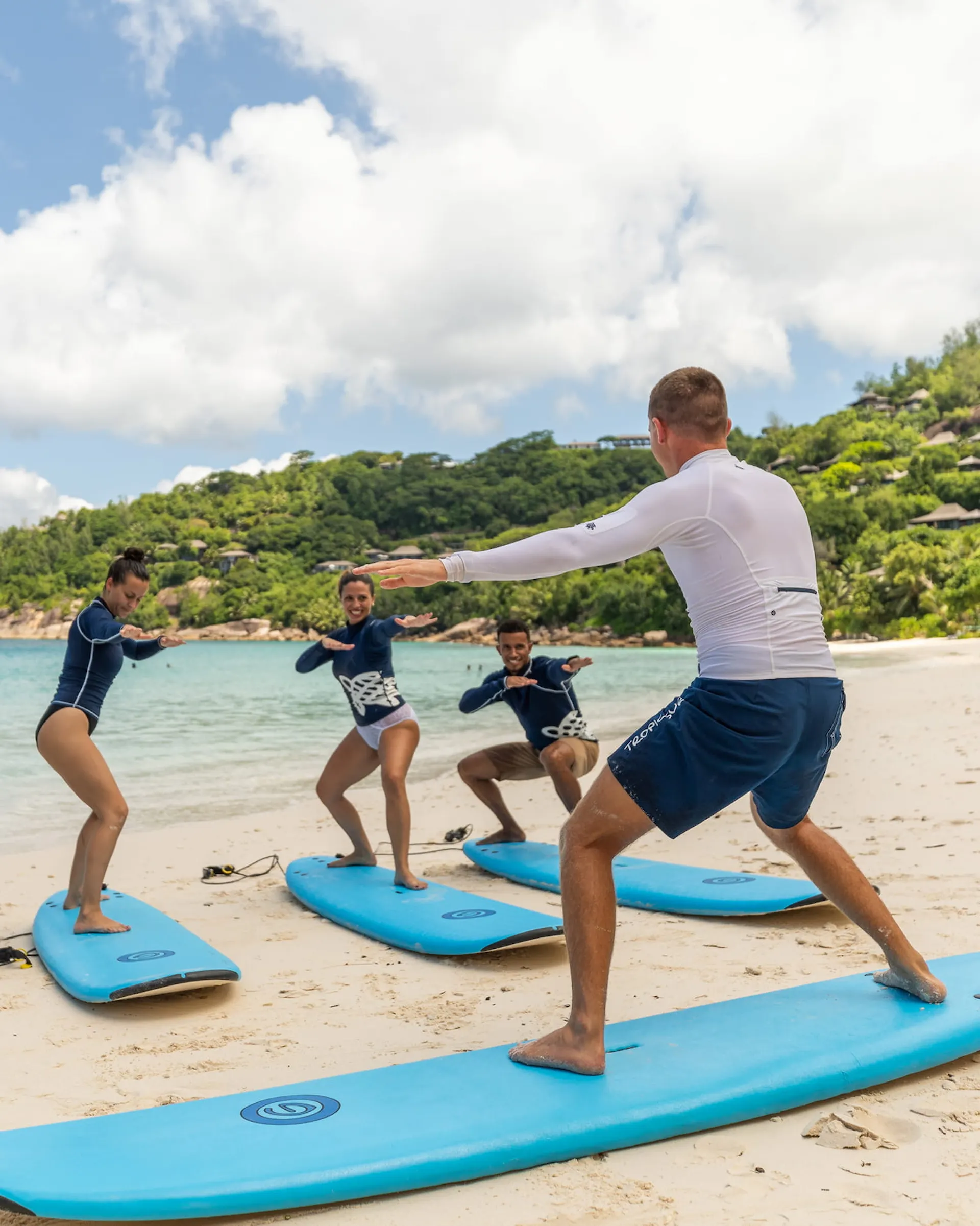 children surfing in gentle waves at Four Seasons Resort Seychelles with tropical beach and ocean backdrop