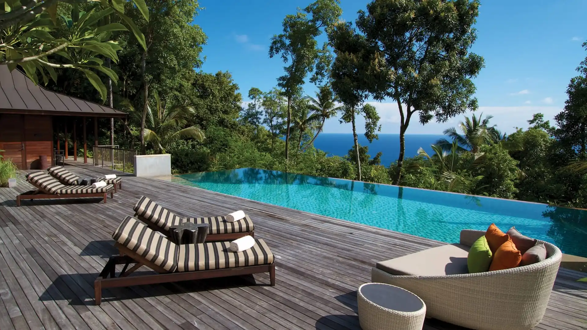 pool decking area with chairs in a three bedroom residence at Four Seasons Resort Seychelles surrounded by tropical greenery and ocean views