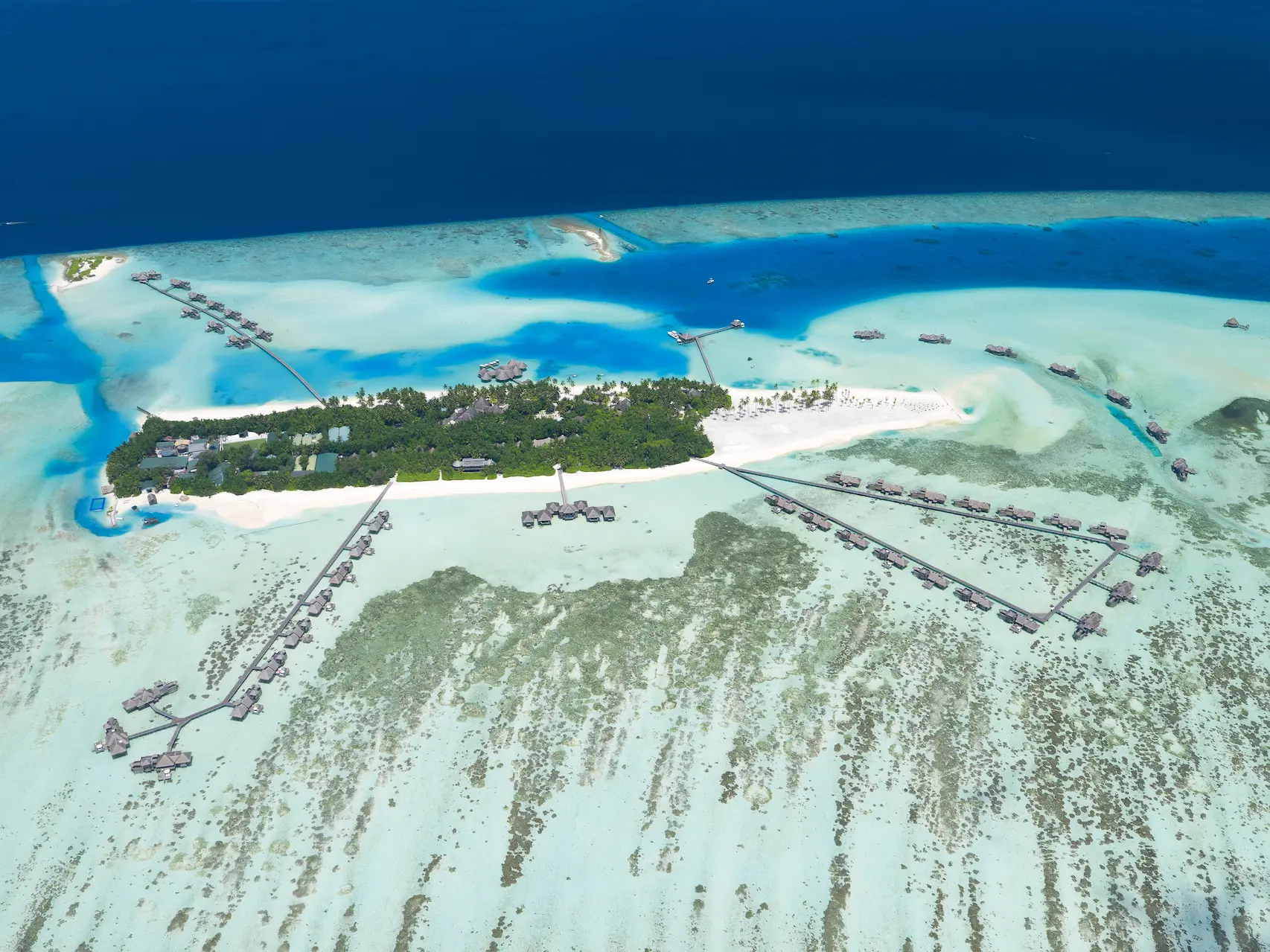 a sweeping aerial shot island view at gili lankanfushi maldives showcasing calm turquoise waters and lush greenery