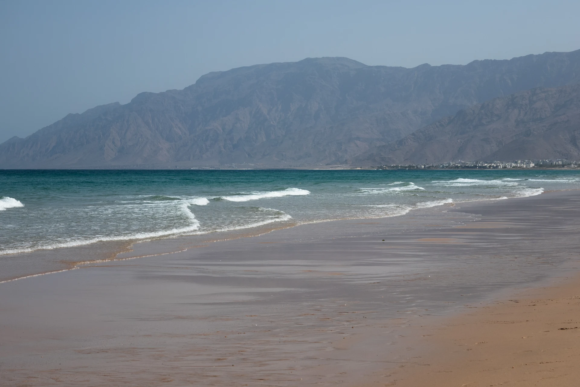 beach at jumeirah muscat bay oman with soft sand calm turquoise sea and scenic coastal mountains surrounding the luxury resort coastline