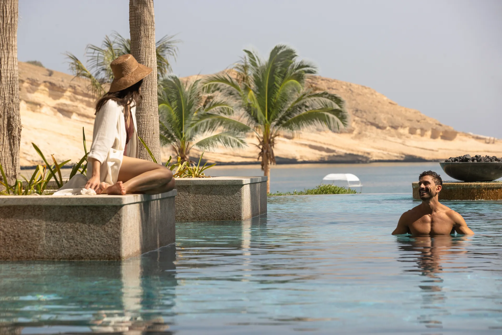 couple at pool at jumeirah muscat bay oman enjoying infinity pool views relaxing sun loungers and luxury coastal resort atmosphere