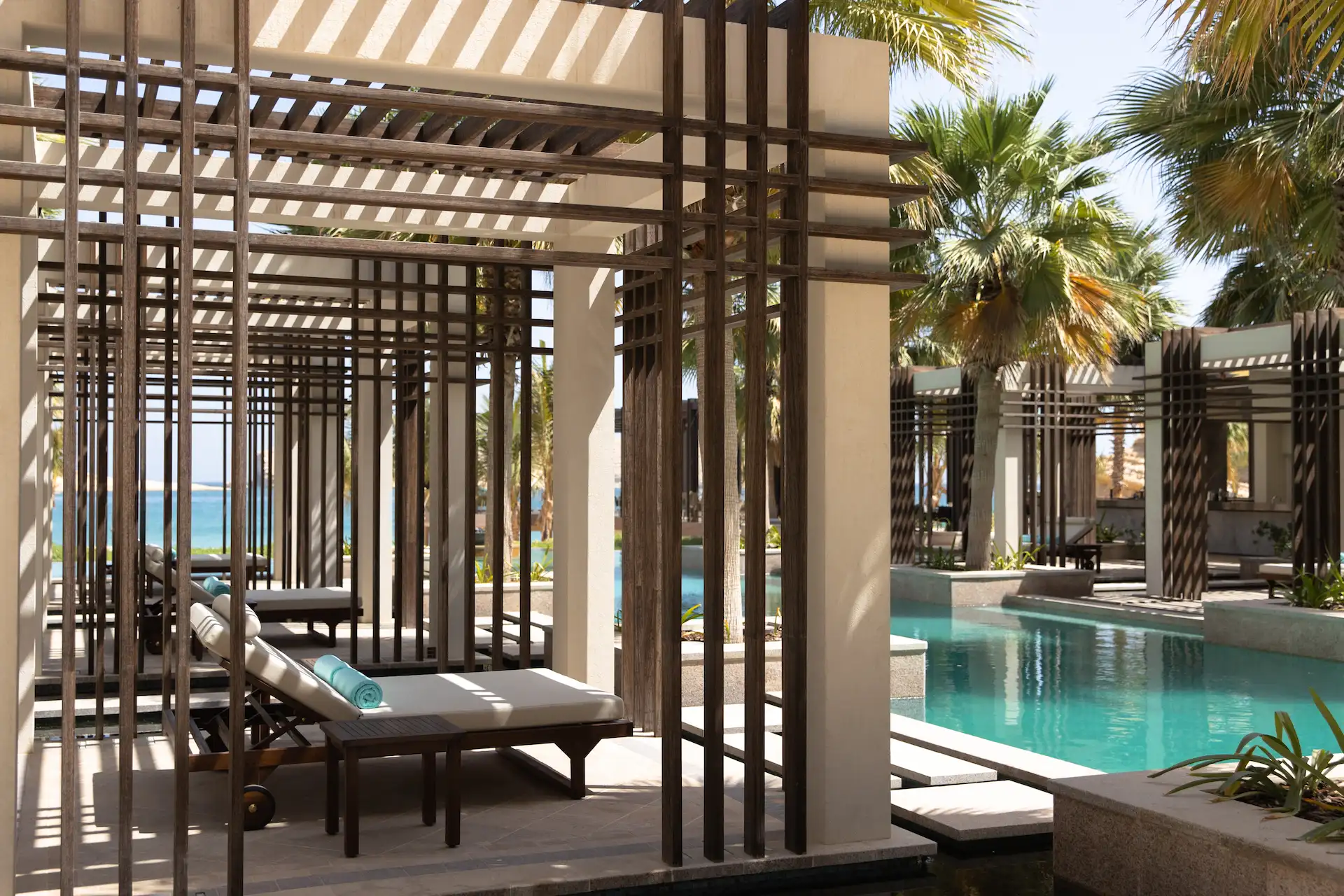 pool lounge at jumeirah muscat bay oman with shaded seating sun loungers and infinity pool views over the coastline