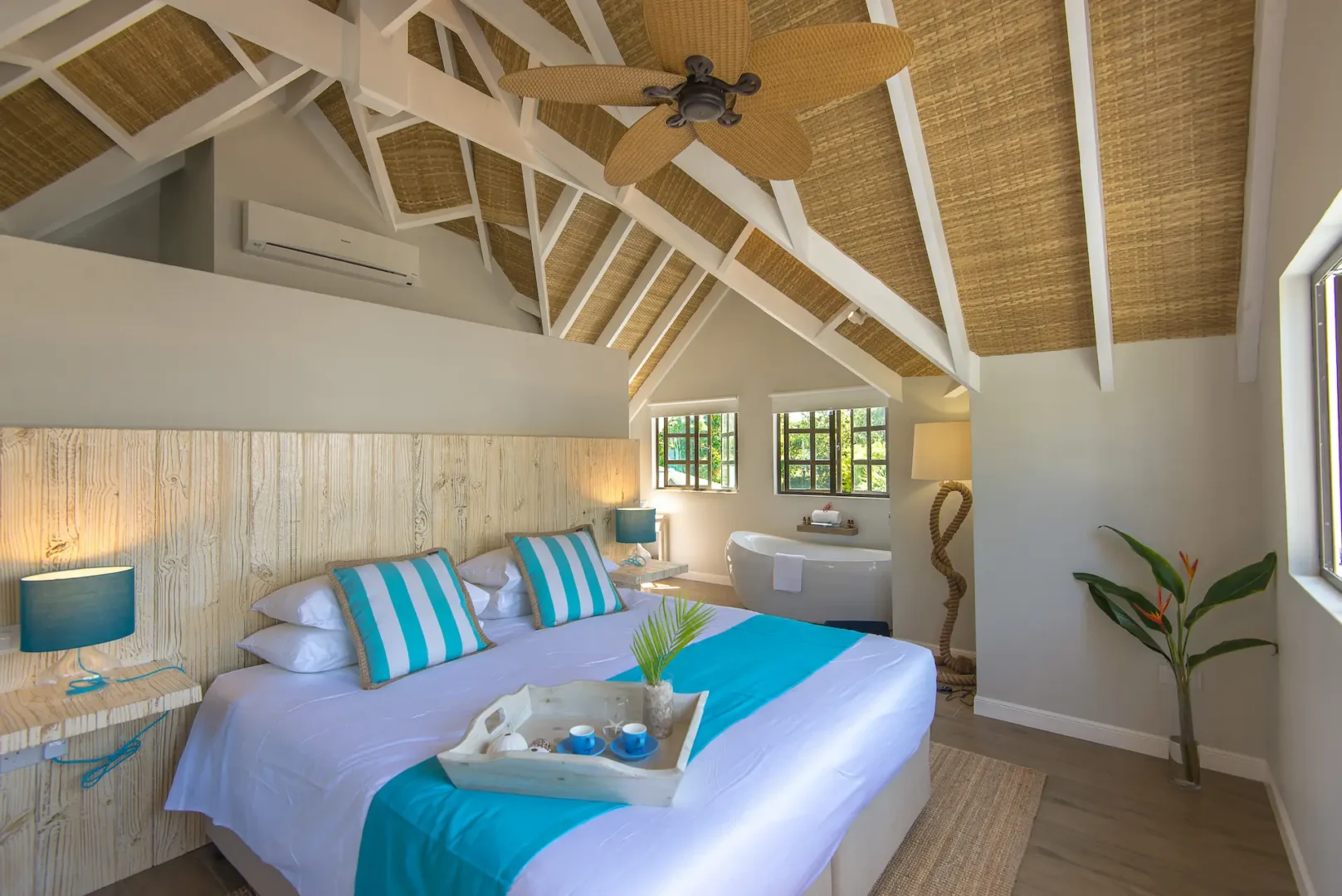 bed in a king deluxe seafront room at Le Nautique with a large bed positioned near windows with views of the ocean and tropical surroundings