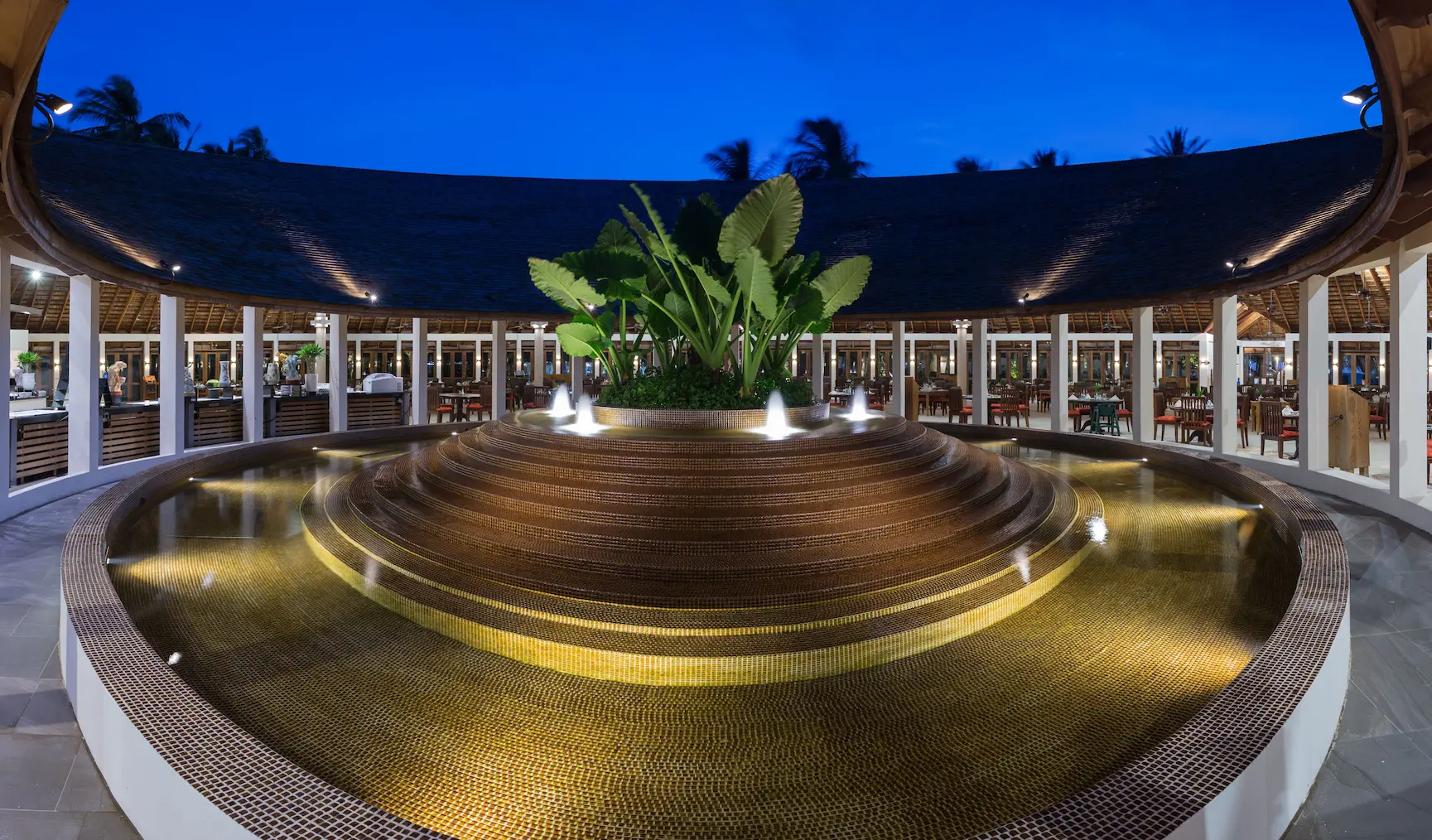 meeru maldives farivalhu restaurant water fountain with gentle ambient lighting tropical greenery and a calm elegant atmosphere enhancing the resort’s relaxed luxury dining setting