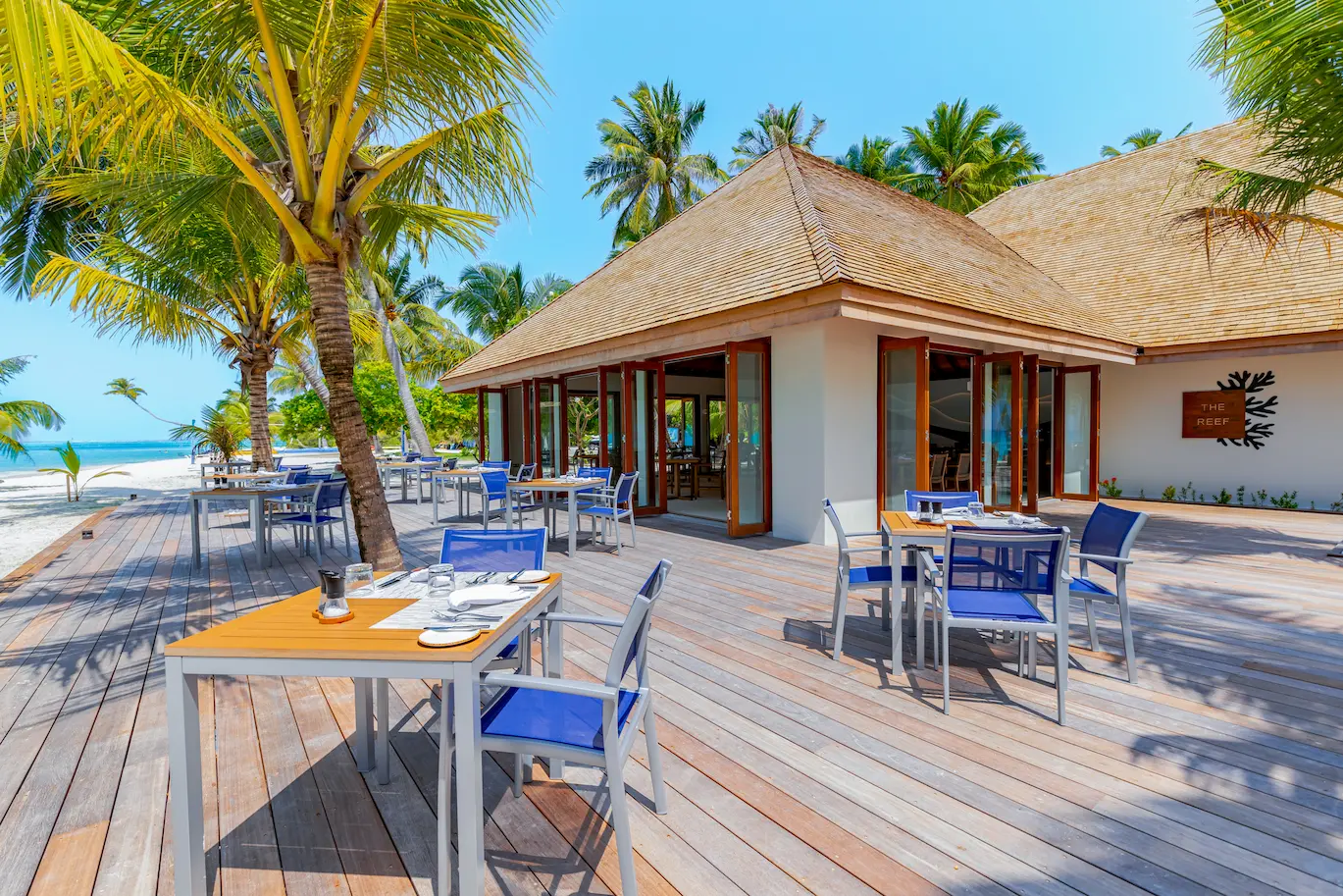 meeru maldives the reef restaurant exterior with soft ambient lighting tropical greenery and a relaxed elegant beachfront dining atmosphere