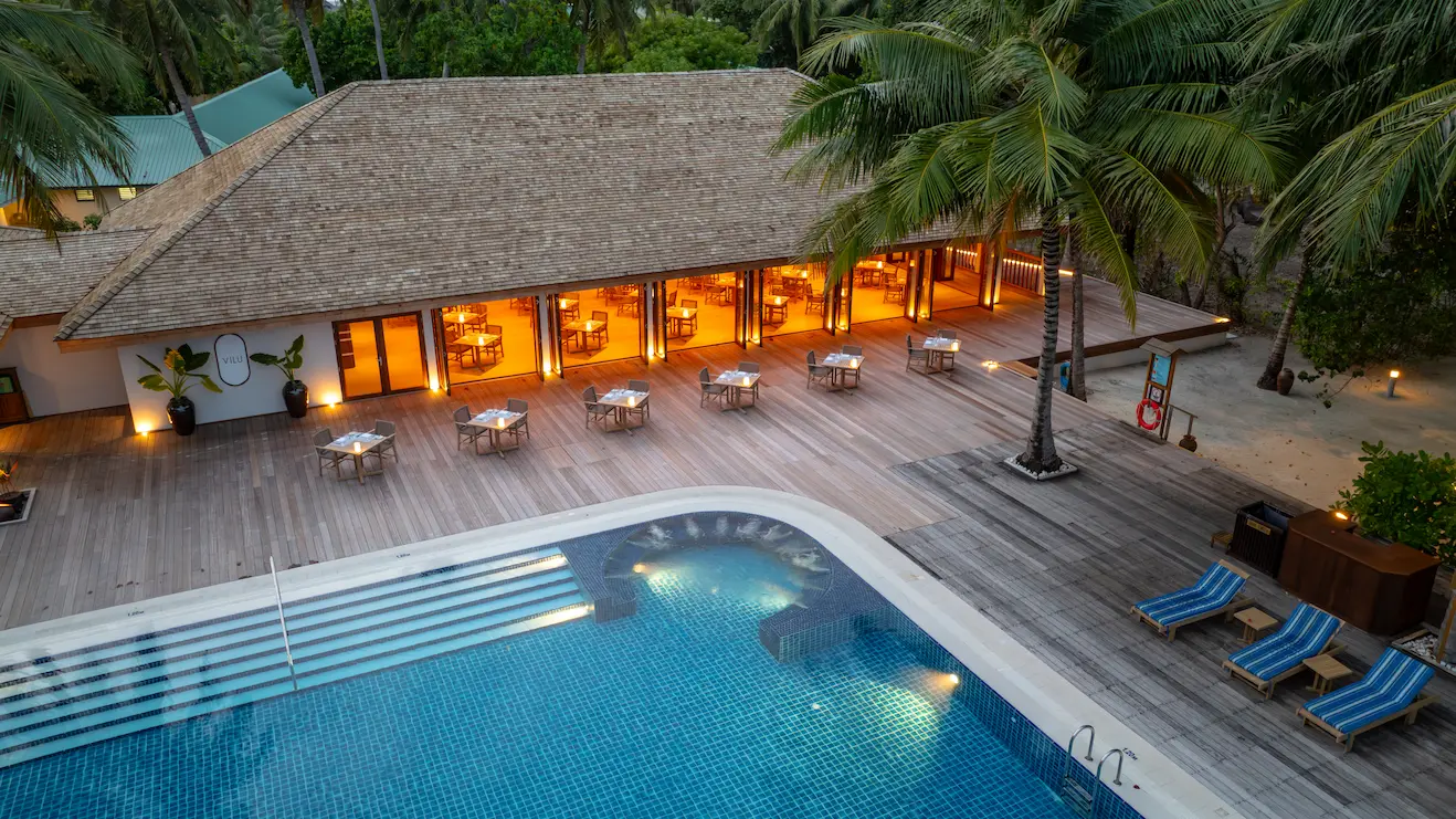 meeru maldives vilu restaurant exterior with warm ambient lighting tropical greenery and a serene beachfront dining atmosphere reflecting the resort’s relaxed luxury style