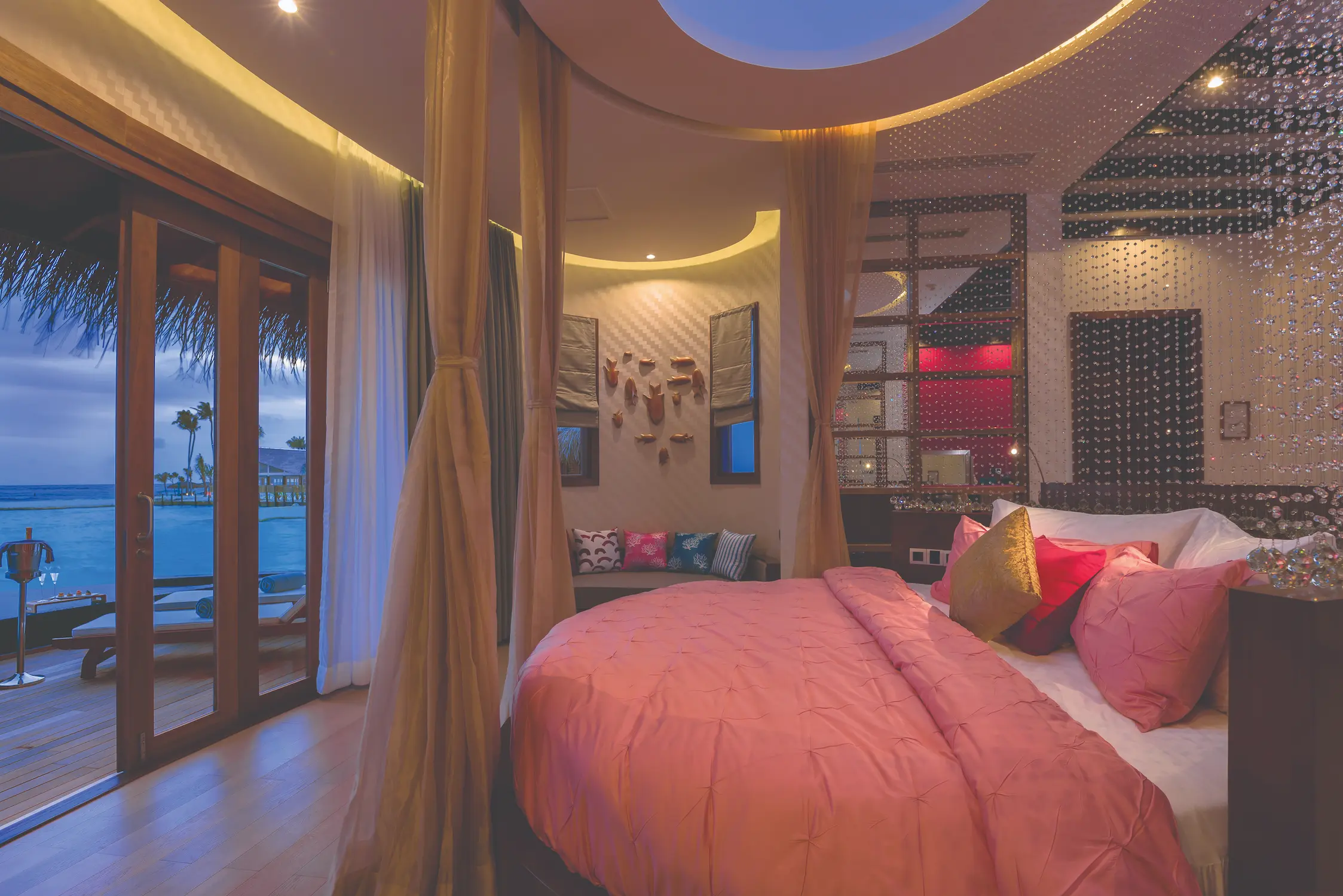 oblu select sangeli maldives honeymoon ocean suite bedroom evening romantic overwater bedroom illuminated with soft evening light warm natural textures and serene lagoon ambience