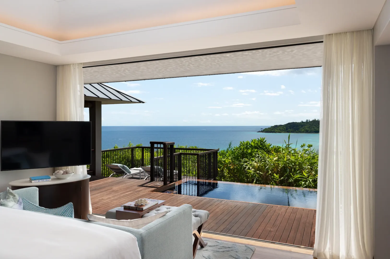 cean view pool villa room in seychelles with seating area, bed, and view