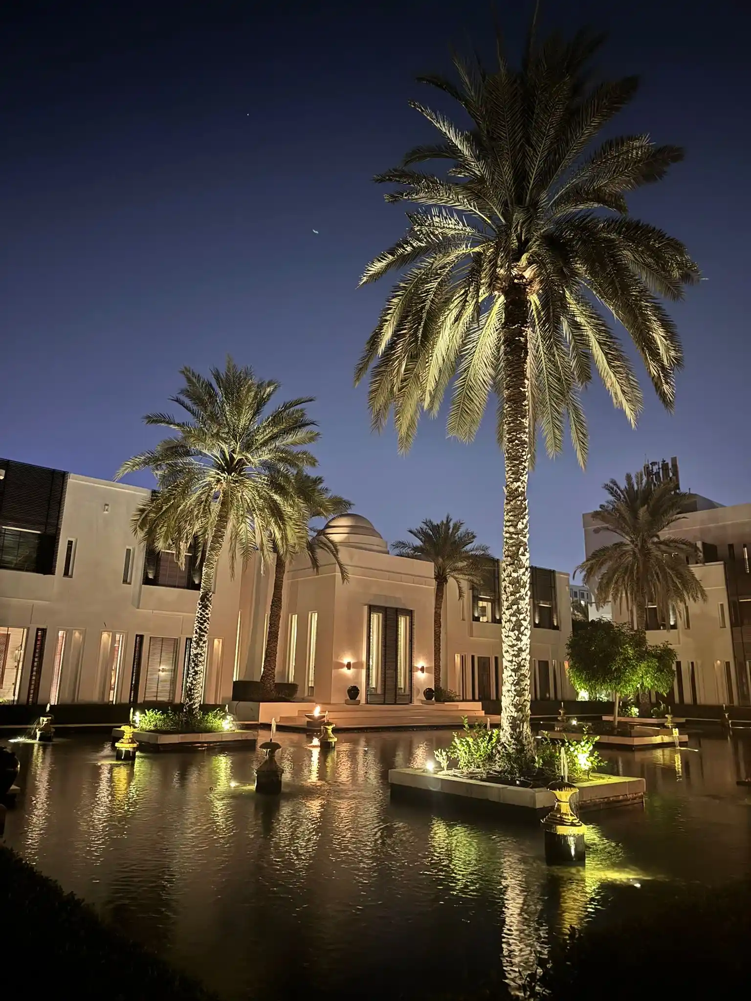 oman the chedi muscat hotel exterior with modern luxury architecture, landscaped gardens, and views of the ocean and surrounding mountains
