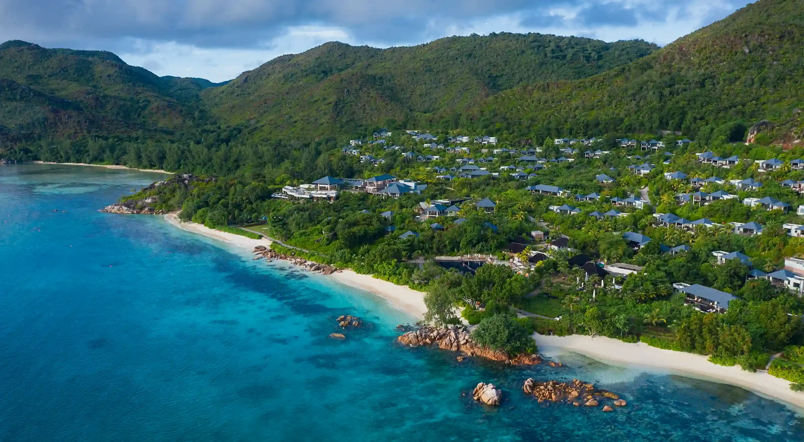 aerial view of raffles seychelles showing overwater and beachfront villas with turquoise ocean and lush greenery