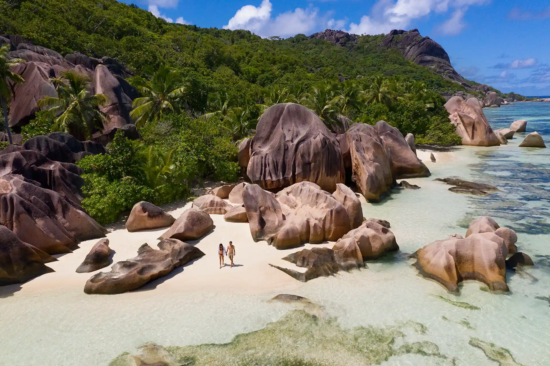 couple on the beach at raffles seychelles with granite rock formations and turquoise water