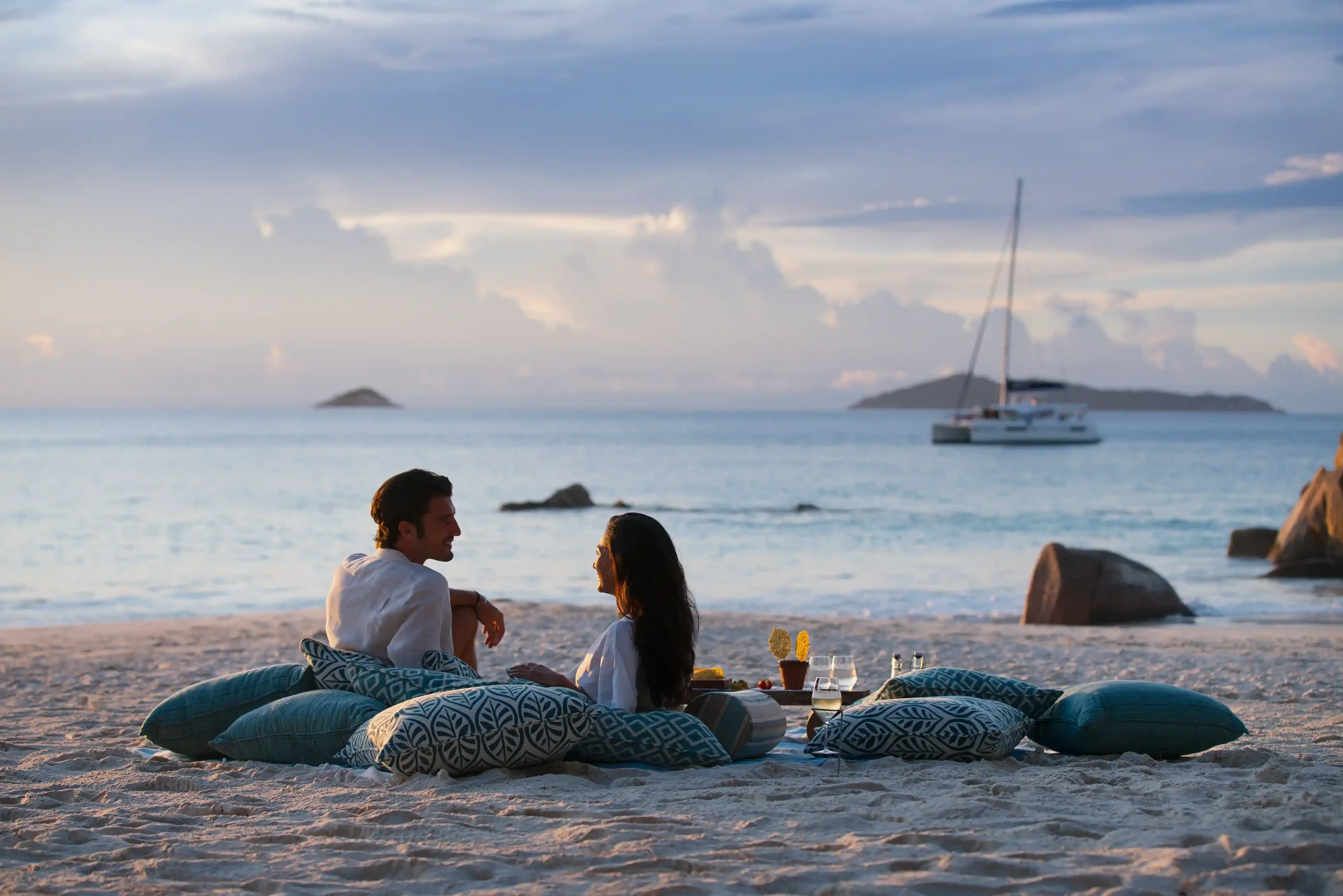 couple walking along the white sand beach at raffles seychelles with turquoise ocean and palm trees