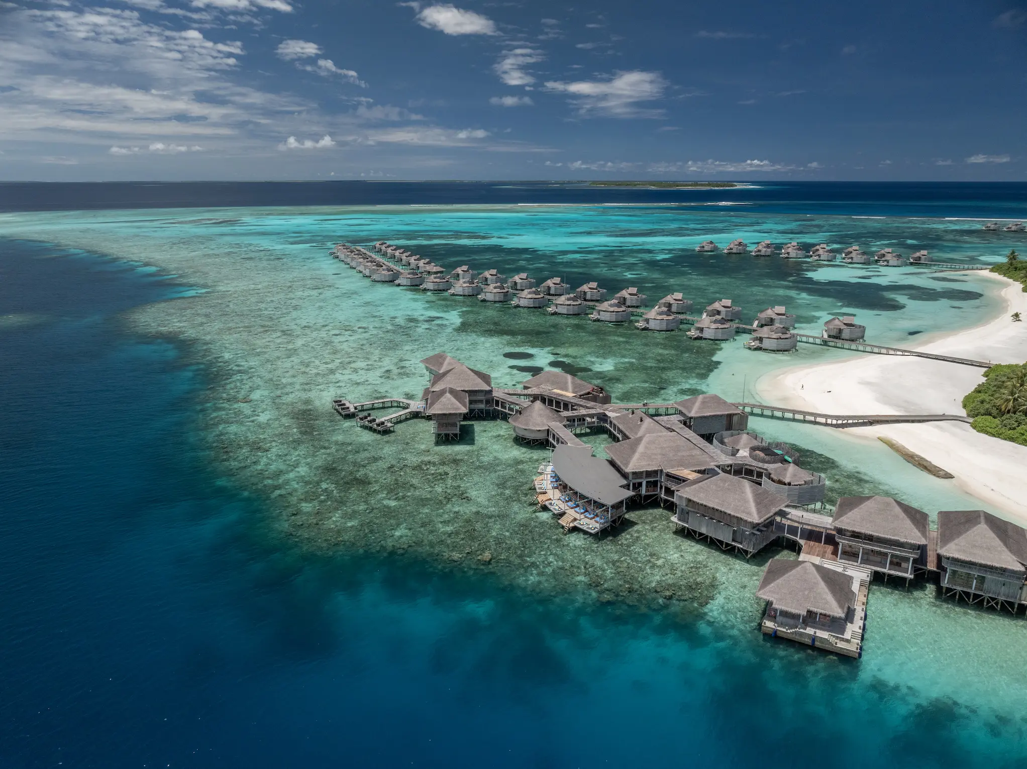 six senses laamu maldives aerial overwater villas above clear turquoise lagoon with natural wood architecture and a serene elevated barefoot luxury atmosphere