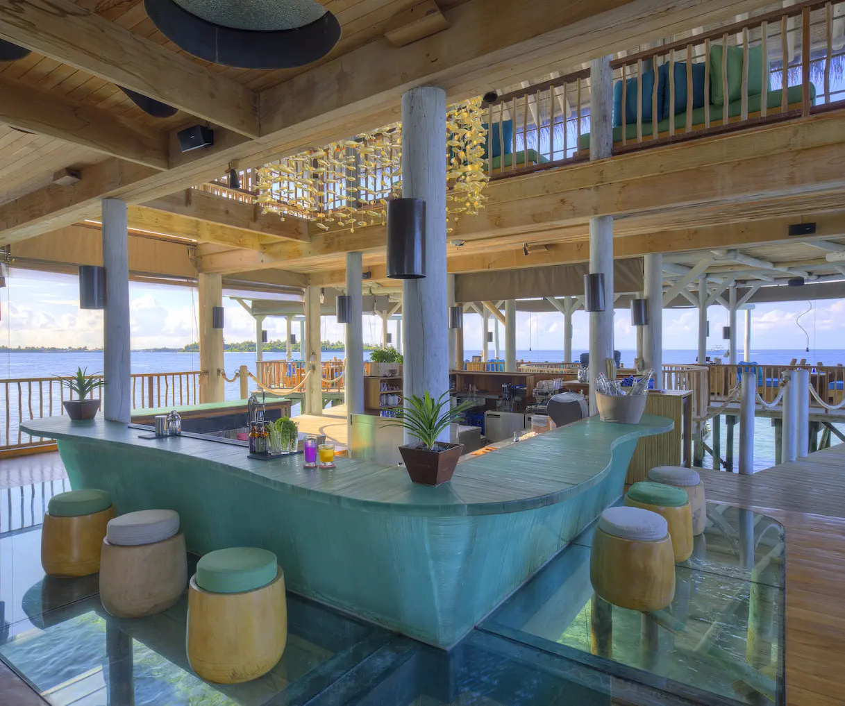 six senses laamu maldives chill bar interior with warm ambient lighting natural wood textures and a calm elevated barefoot luxury atmosphere
