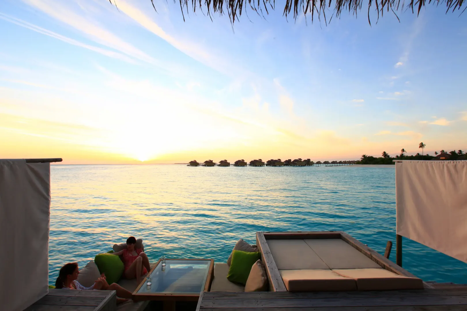 six senses laamu maldives ocean water villa deck at sunset with warm golden light over the lagoon and a tranquil refined luxury atmosphere