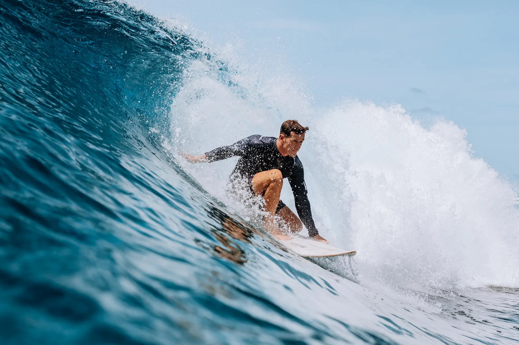 six senses laamu maldives surfing over clear turquoise waves with gentle ocean breeze and a dynamic elevated barefoot luxury adventure atmosphere