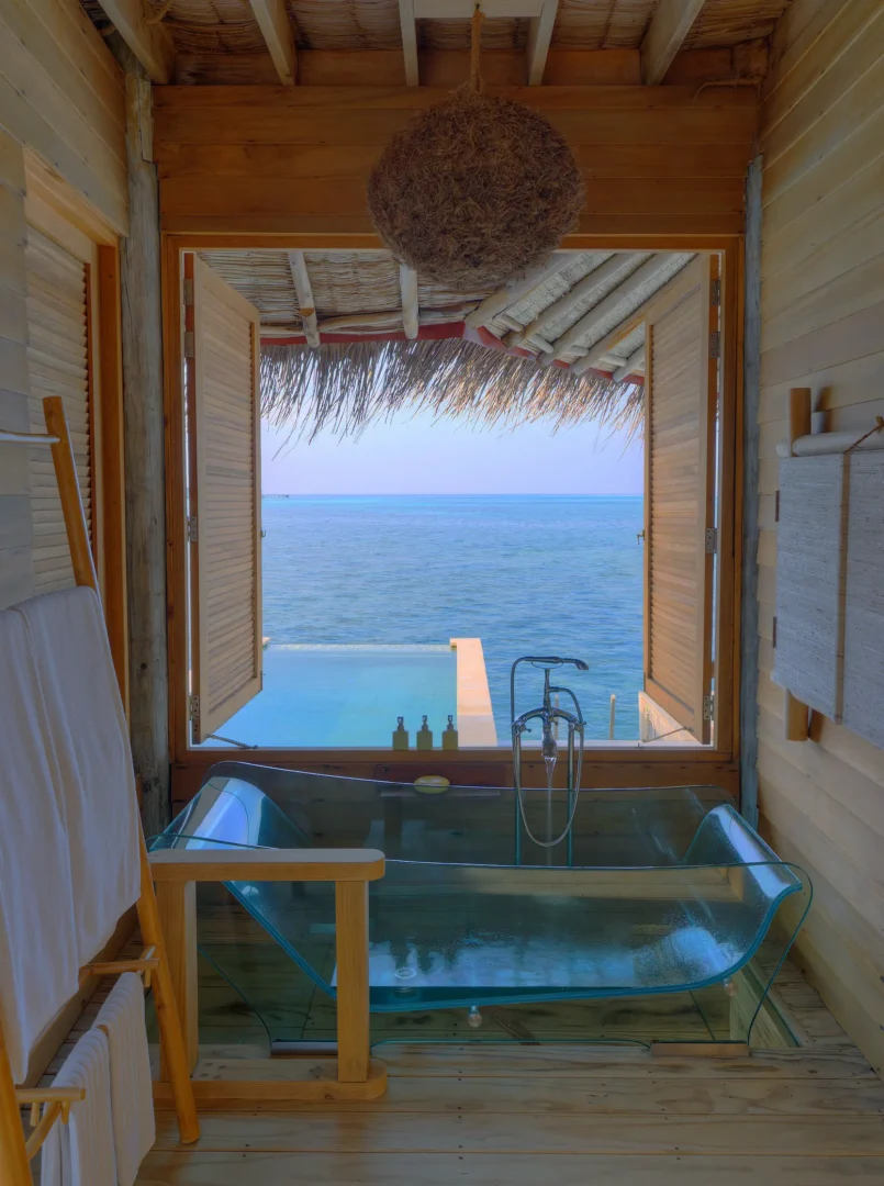 six senses laamu maldives water villa with pool bathroom featuring natural wood textures soft ambient lighting and a calm refined barefoot luxury atmosphere