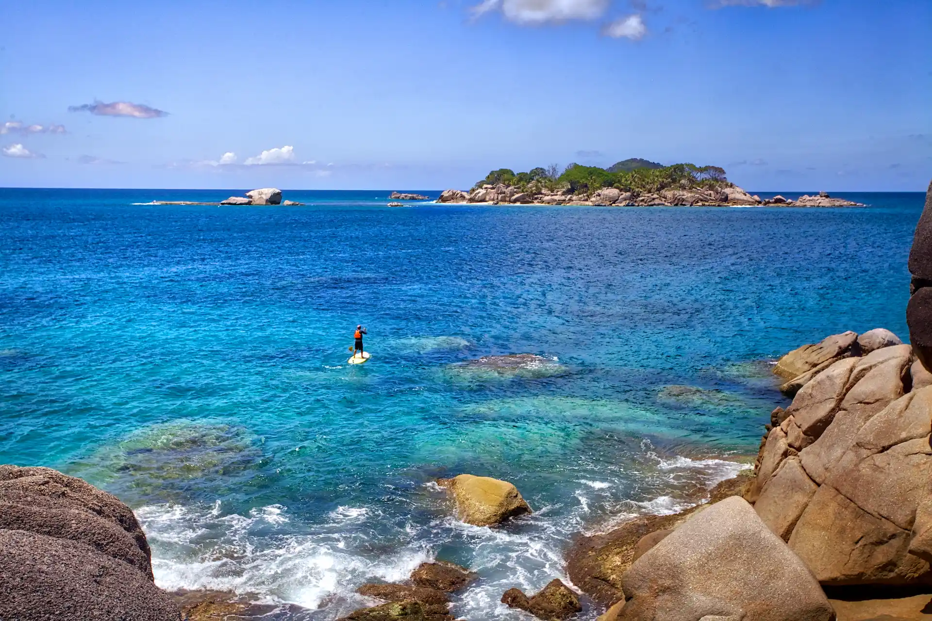person standup paddling on clear blue ocean at six senses seychelles