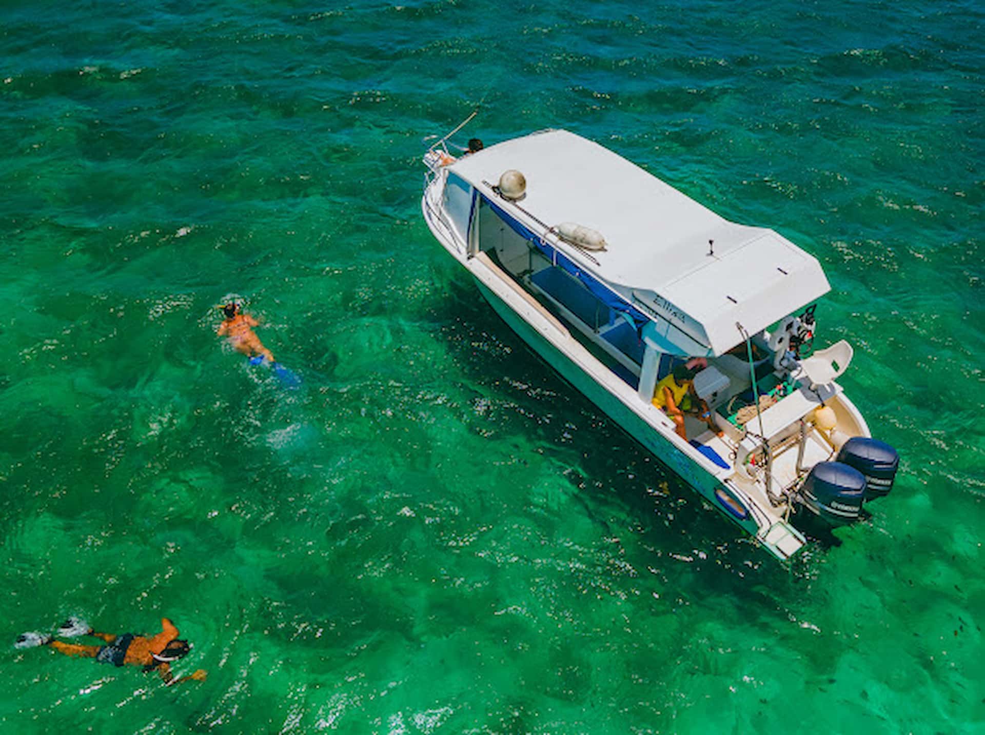 A small boat anchored near crystal-clear waters in Seychelles, with people preparing for snorkelling