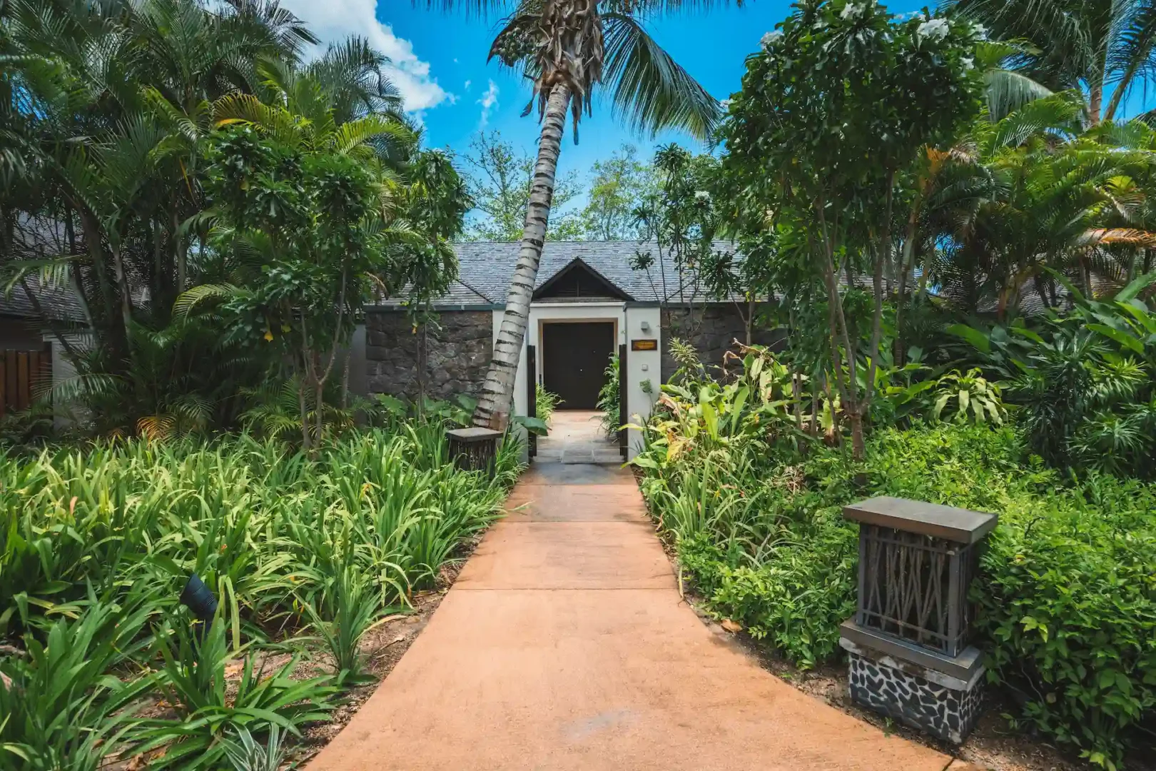 Entrance to a grand beach pool villa in Seychelles, with a private pathway leading into the property surrounded by tropical greenery