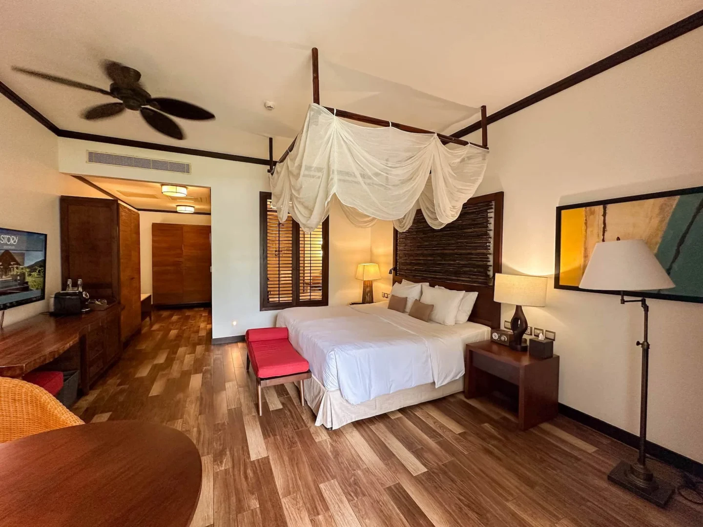 Bedroom of a junior suite with balcony in Seychelles, featuring a large bed, tropical decor, and natural light from the balcony doors.