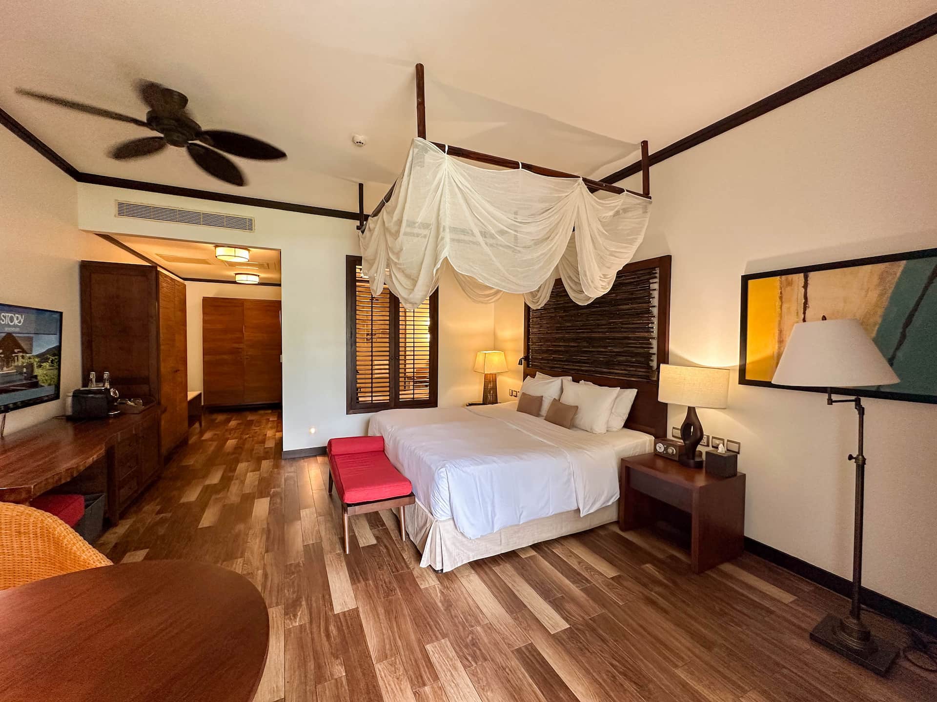 Bedroom of a junior suite with balcony in Seychelles, featuring a large bed, tropical decor, and natural light from the balcony doors.