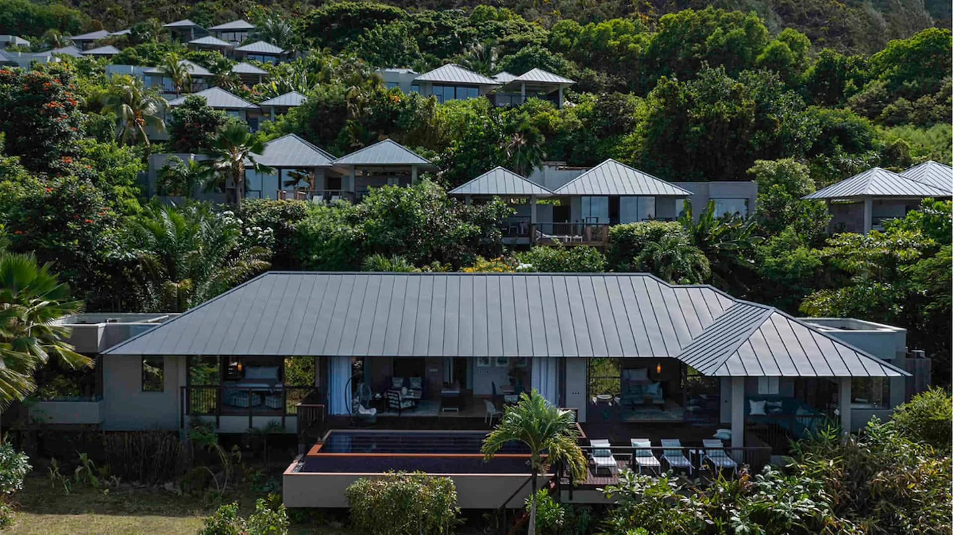 exterior view of two bedroom beachfront pool villa in seychelles with tropical birds flying over white sand beach and turquoise sea