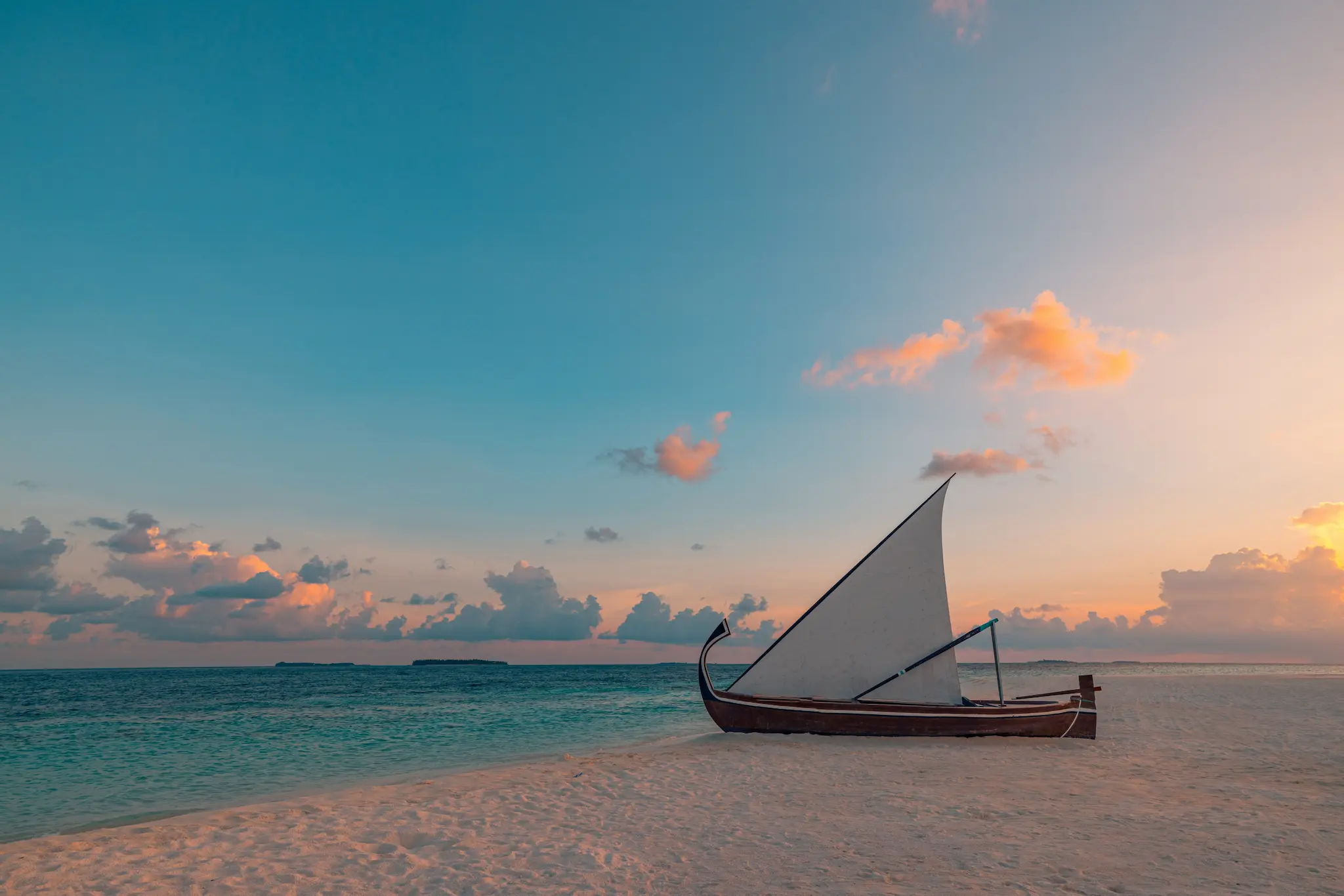 sun siyam vilu reef maldives beach sunset with warm golden light reflecting across white sand and calm shoreline