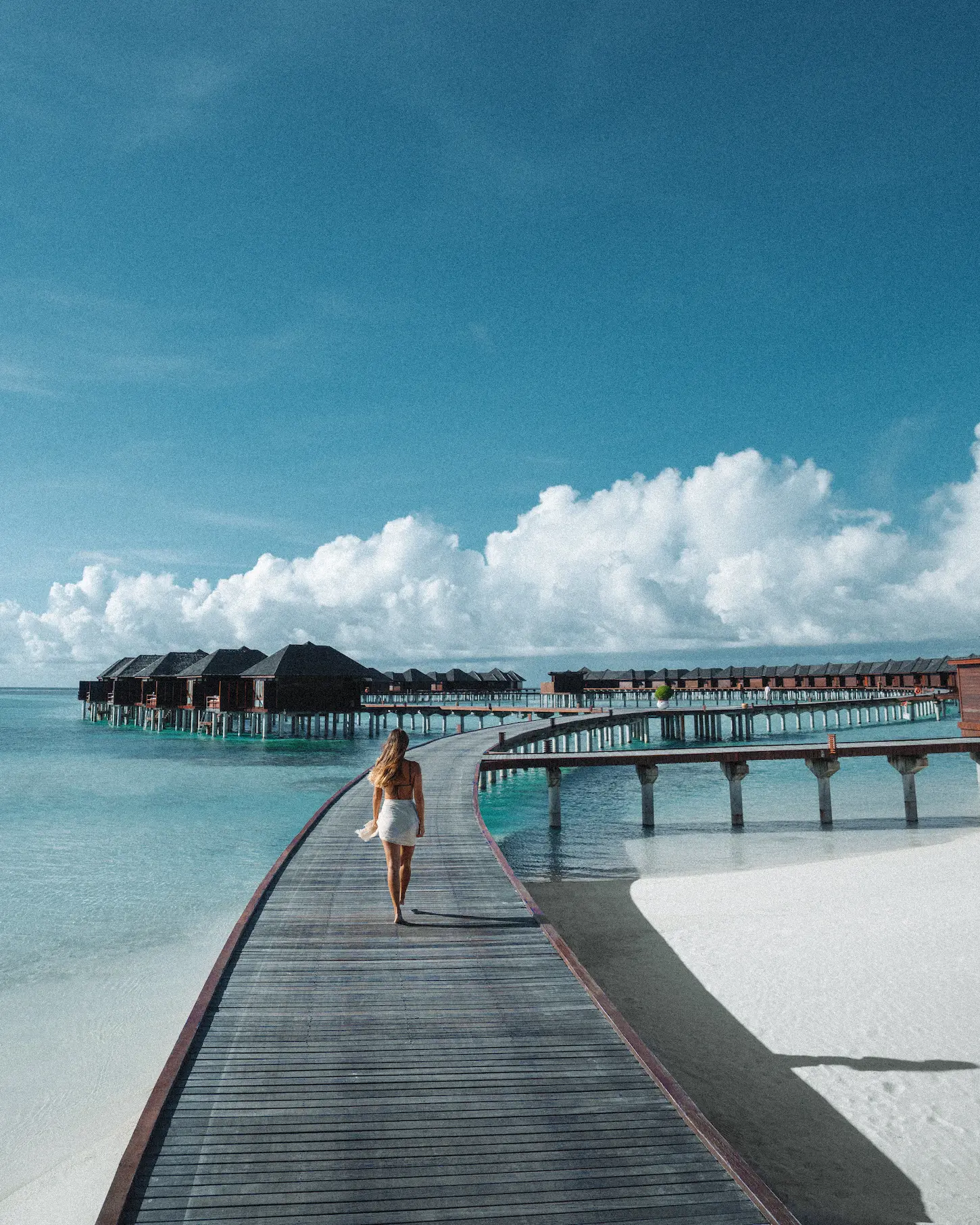 guests walking along an overwater jetty at sun siyam olhuveli maldives with views across the lagoon and water villas