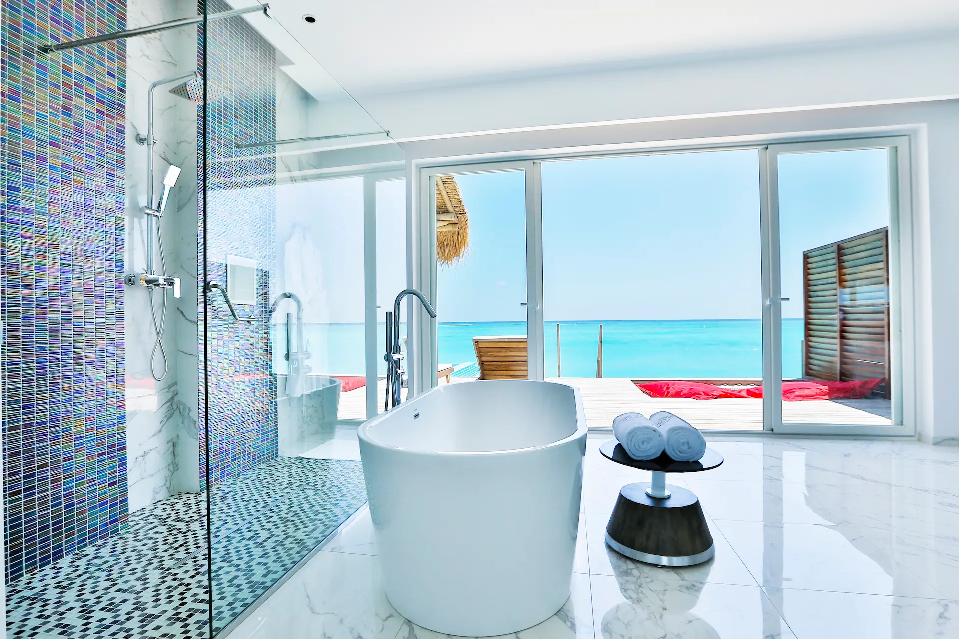 bathroom in a water villa at emerald maldives resort & spa in the maldives featuring a bathtub, walk-in shower and views towards the overwater sundeck