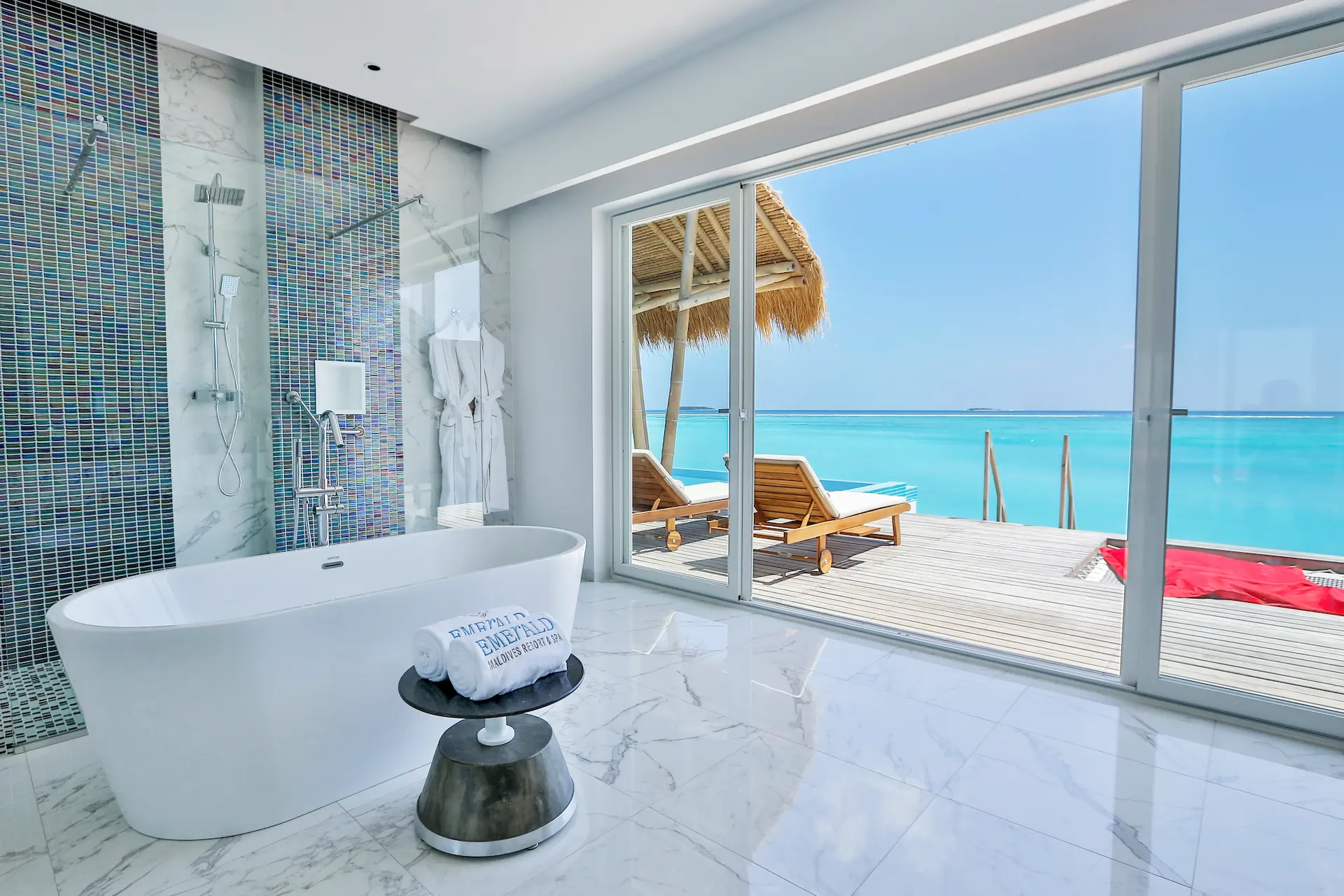 bathroom in a water villa with pool at emerald maldives resort & spa in the maldives featuring a bathtub, walk-in shower and views towards the private overwater sundeck and pool
