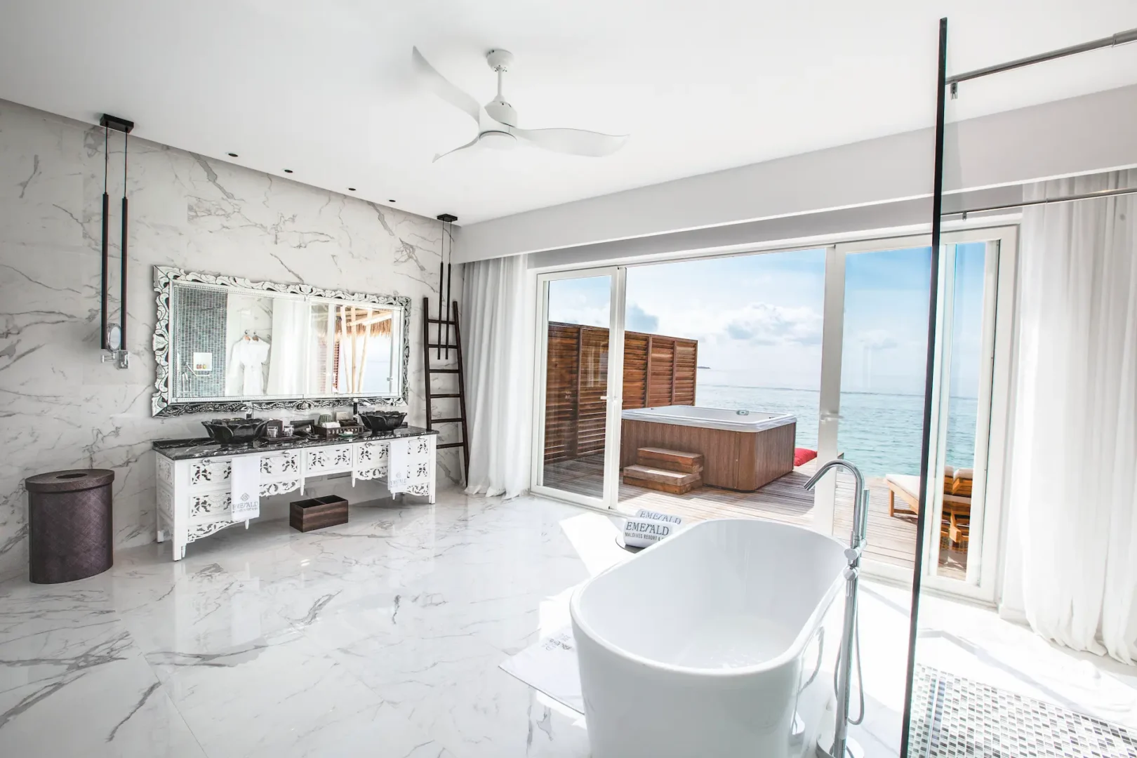 bathroom in a jacuzzi water villa at emerald maldives resort & spa in the maldives featuring a bathtub, walk-in shower and views towards the overwater sundeck and private outdoor jacuzzi