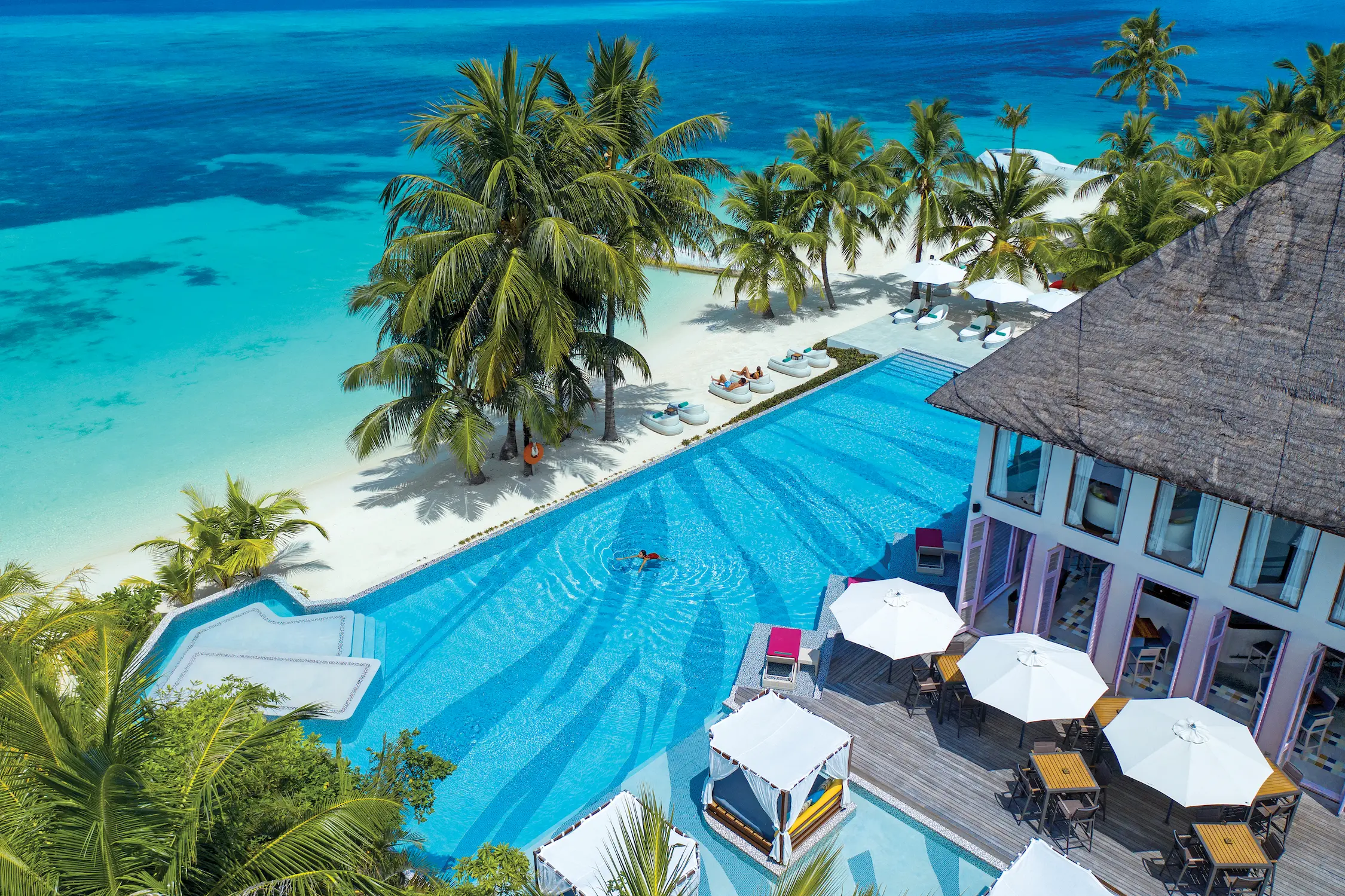 Aerial view of Joie De Vivre at OZEN LIFE MAADHOO, showcasing the lagoon-facing pool area, pool bar and central social hub overlooking the ocean