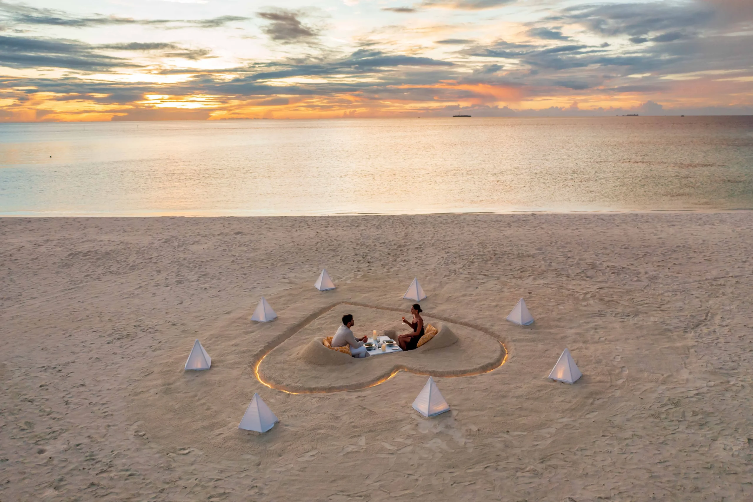 Private beachfront dining experience at OZEN LIFE MAADHOO, featuring an elegantly arranged table on the sand with ocean views and personalised service.