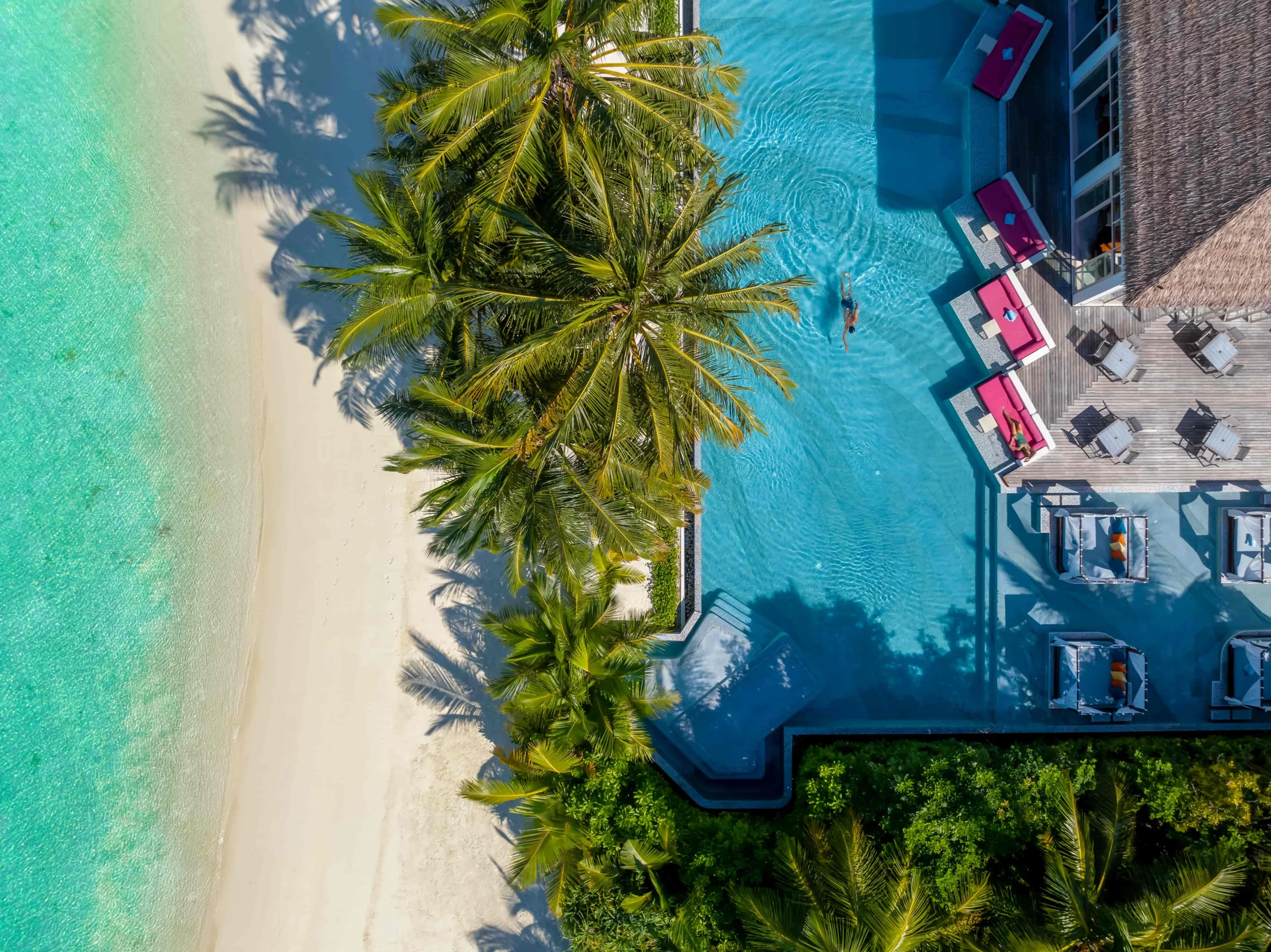 Guests relaxing in the main infinity pool at OZEN LIFE MAADHOO, enjoying lagoon views from the resort's central pool area overlooking the Indian Ocean.
