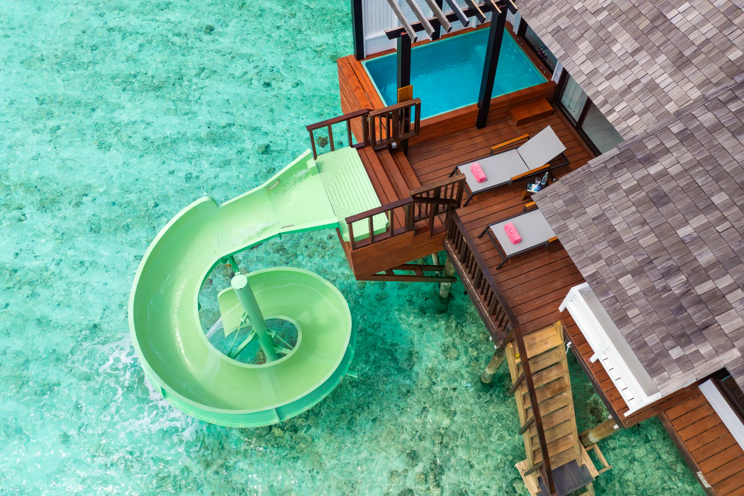 Aerial view of the private deck at a Wind Villa with Jacuzzi & Slide at OZEN LIFE MAADHOO, featuring an overwater setting, outdoor Jacuzzi, waterslide and direct lagoon access