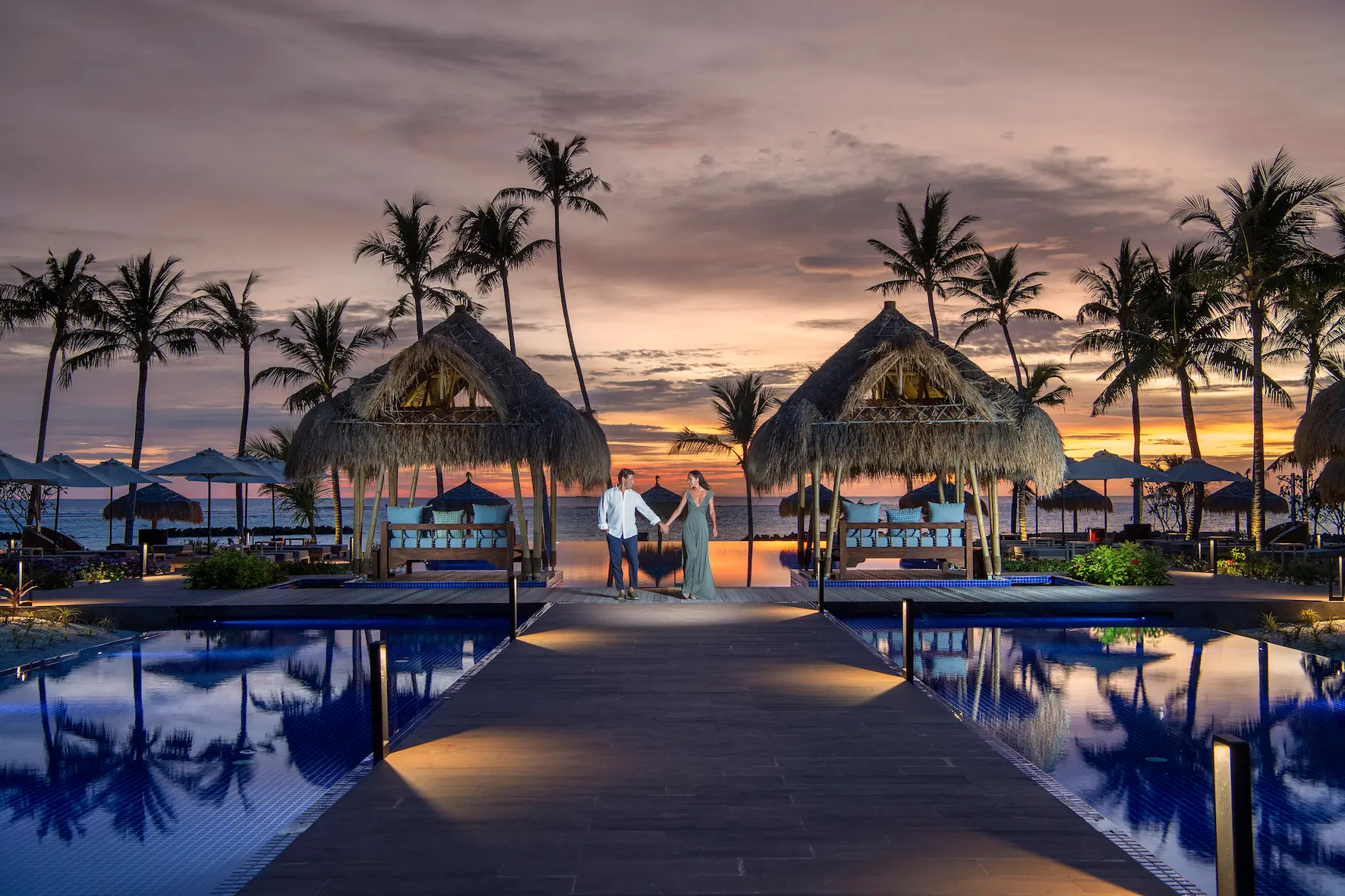 main swimming pool at emerald maldives resort & spa in the maldives illuminated at night with surrounding seating areas and lagoon views